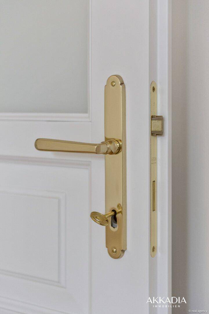 Detail einer weißen Kassettentür mit einem eleganten goldenen Türgriff und Schloss.