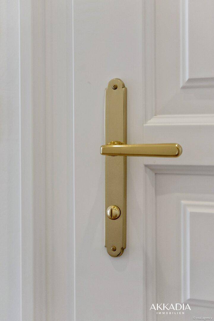 Detailaufnahme einer weißen Tür mit eleganter goldener Klinke und klassischer Paneelierung.