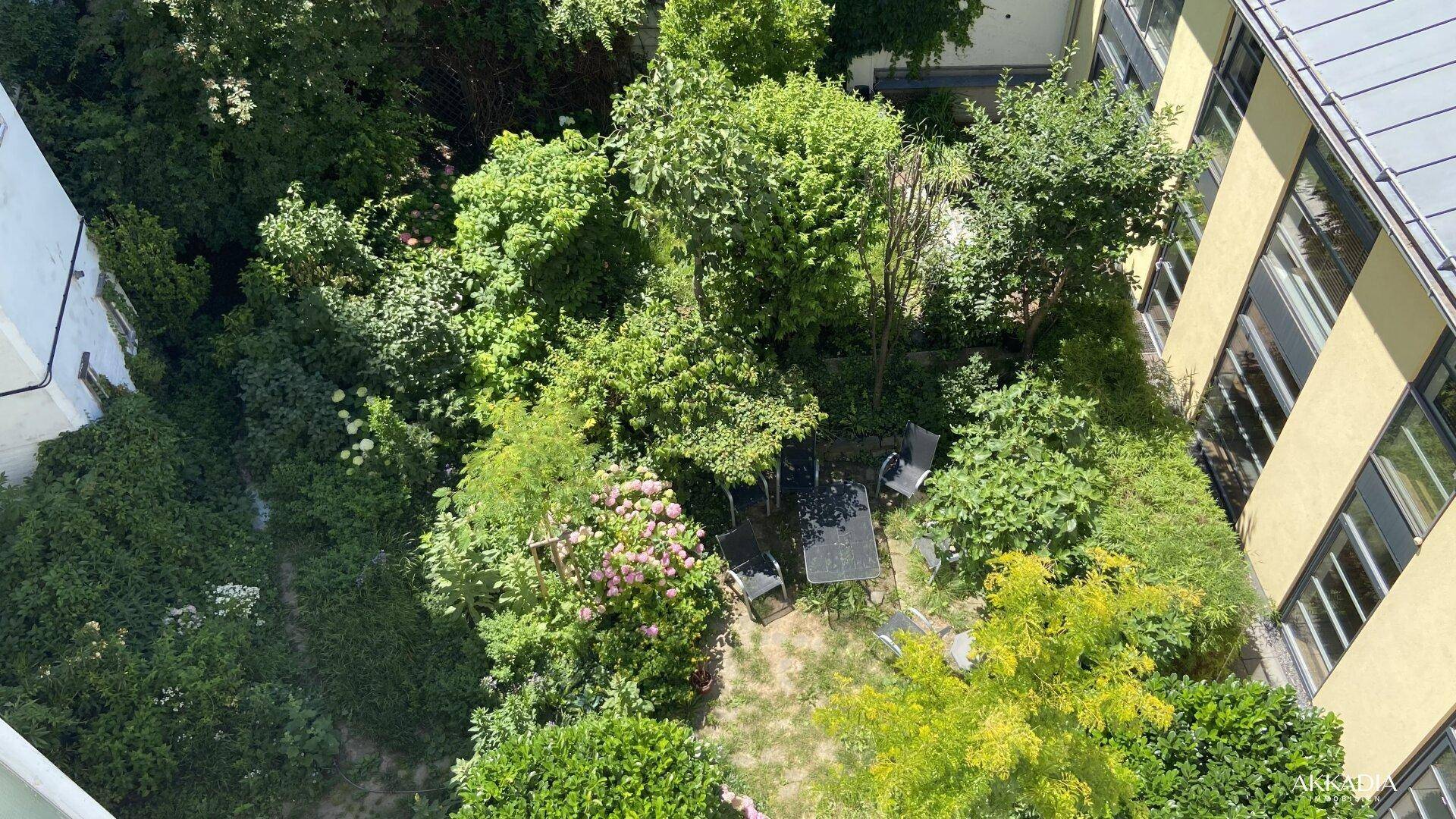 Blick von oben auf einen grünen Innenhof mit Sitzbereich, umgeben von Bäumen und Gebäuden.