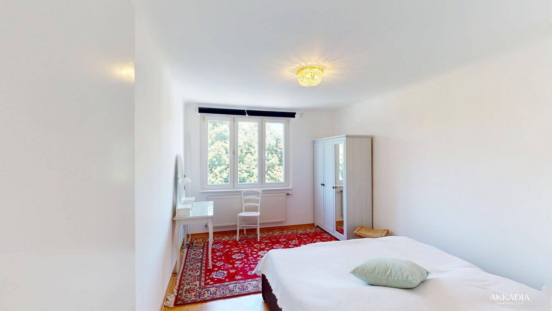 Schlafzimmer mit Doppelbett, weißem Kleiderschrank und einem Fenster mit Blick ins Grüne.