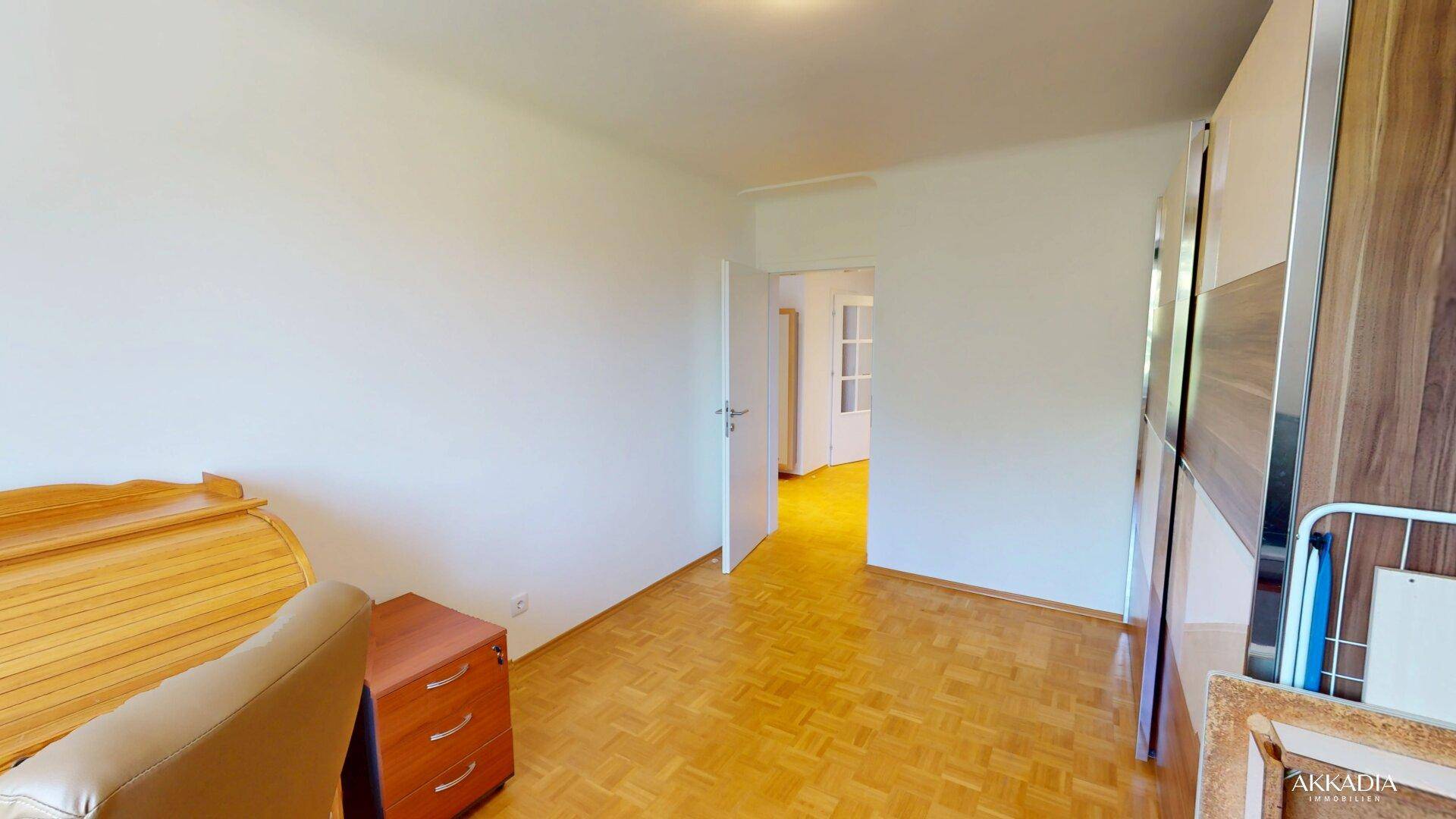Heller Raum mit Parkettboden und einem großen Kleiderschrank, offene Tür führt in den nächsten Bereich.