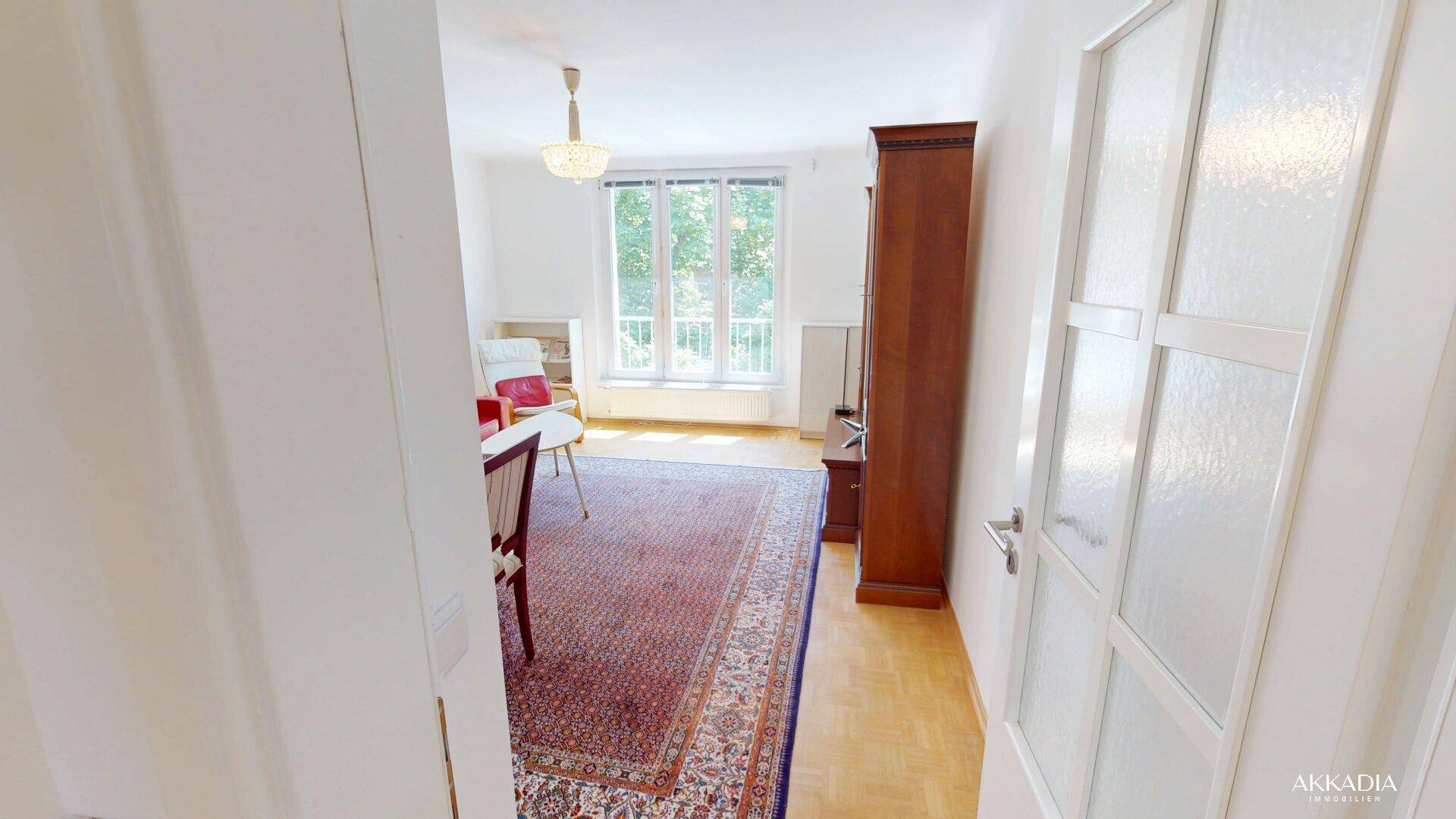 Flur mit Milchglastür, der in ein helles Wohnzimmer mit Parkettboden führt.