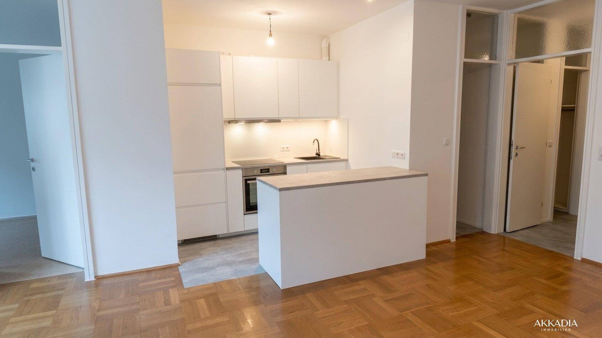 Moderne Einbauküche mit weißen Schränken, integrierten Geräten und Parkettboden.