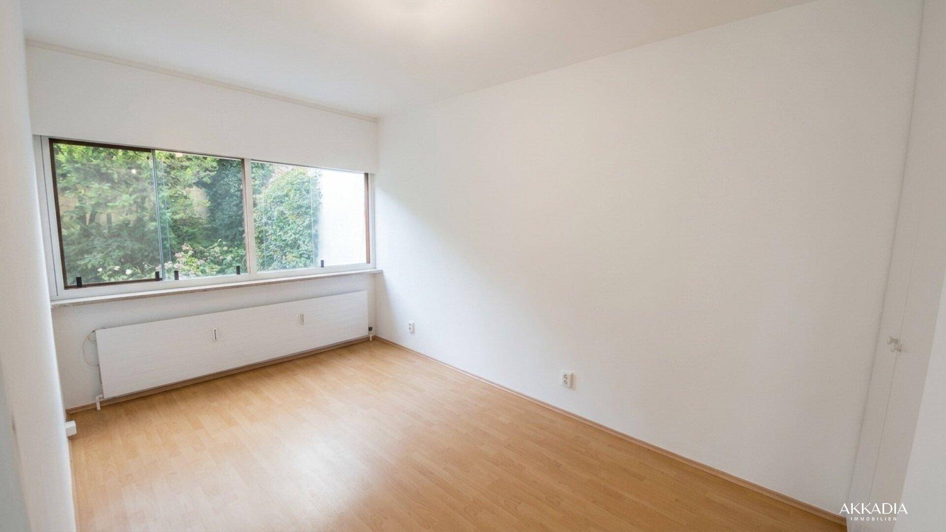 Helles Zimmer mit Laminatboden und großem Fenster mit Blick ins Grüne.