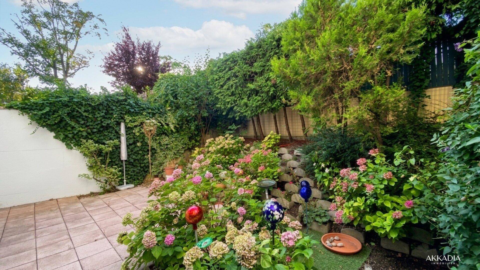 Gepflegter Garten mit blühenden Hortensien und einer kleinen Terrasse.