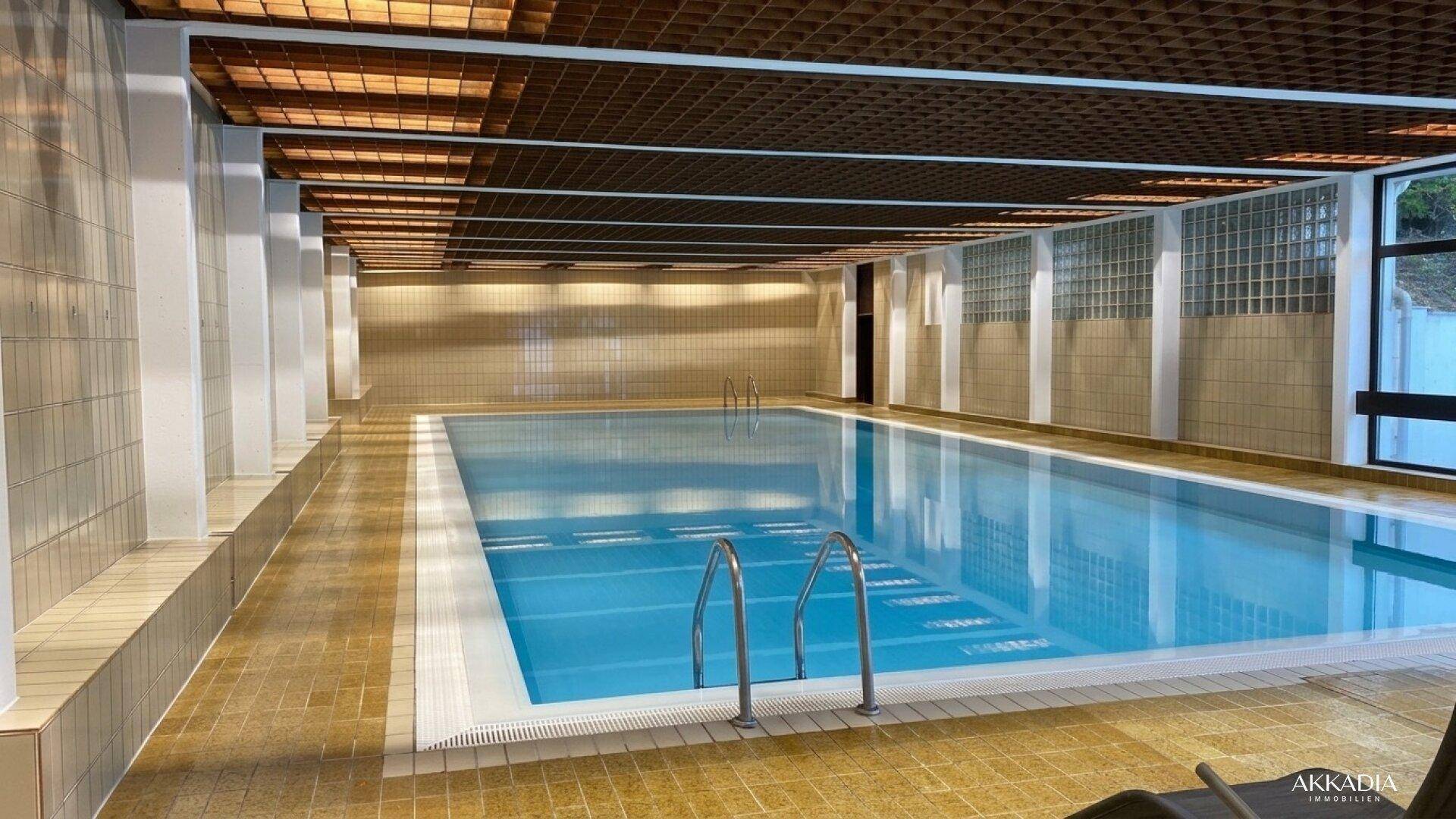 Großes Hallenbad mit gefliestem Becken und Holzdeckenverkleidung.