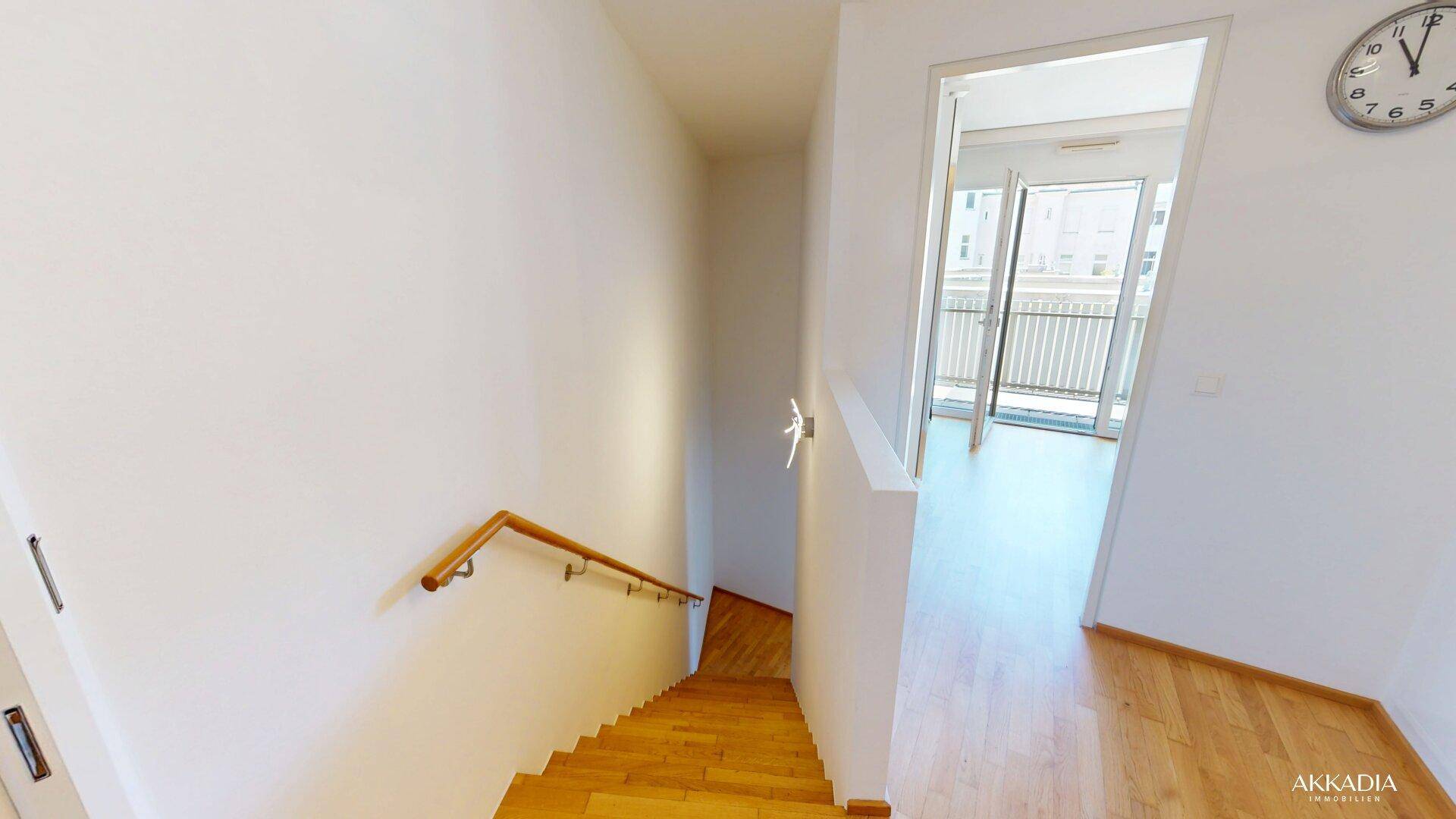 Heller Flur mit Holztreppe, die in die obere Etage führt, und Blick auf einen Balkon.