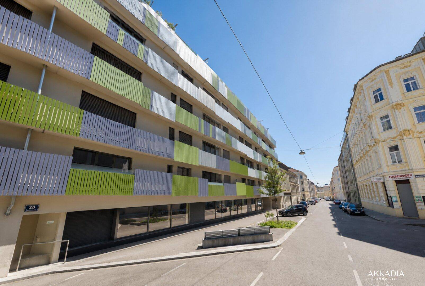 Moderne Wohnhausfassade mit farbigen Balkonverkleidungen und großen Fenstern an einer Straße.