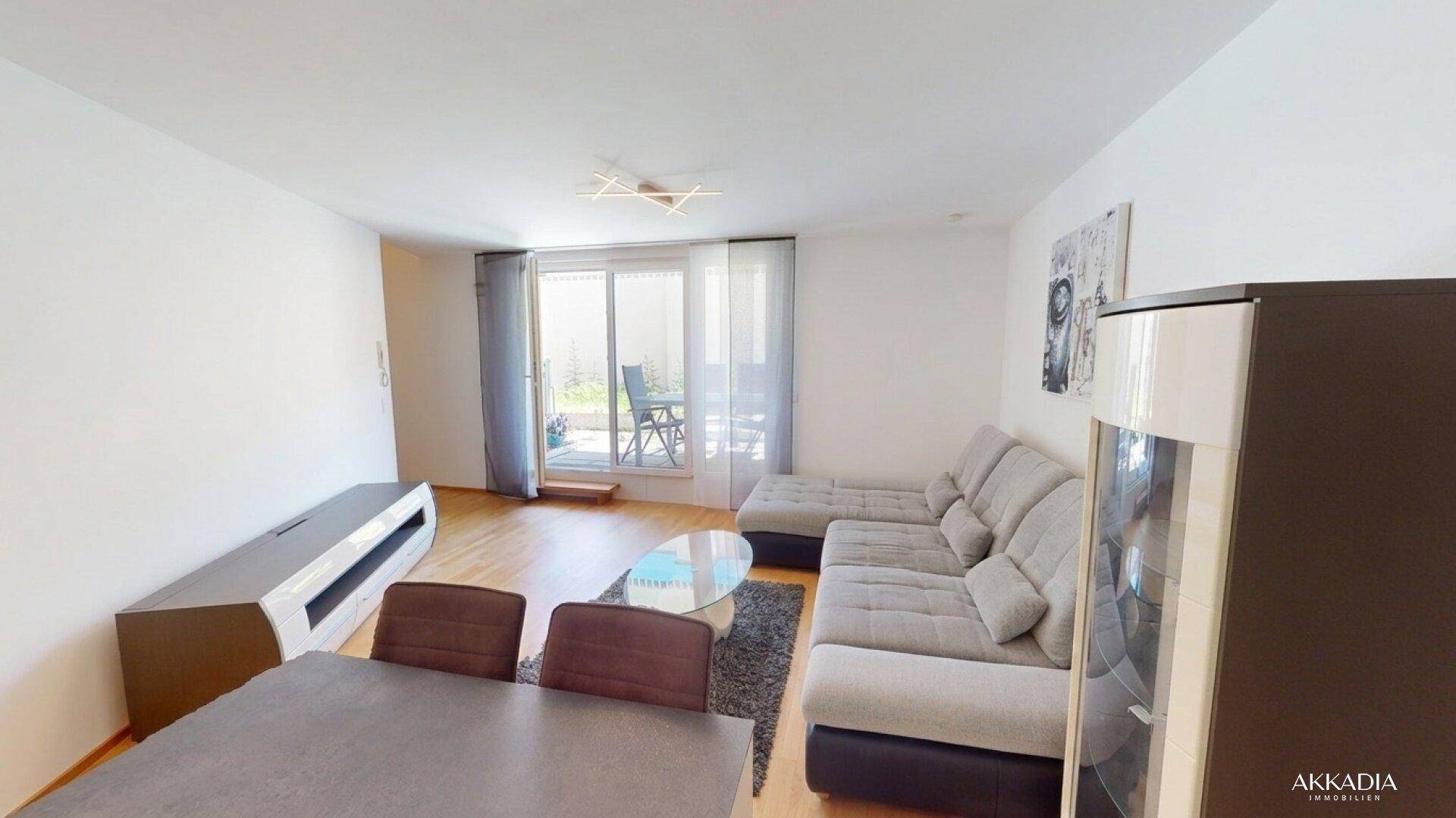 Geräumiger Wohnbereich mit bequemer Couch, Esstisch und Zugang zur Terrasse durch große Fenster.