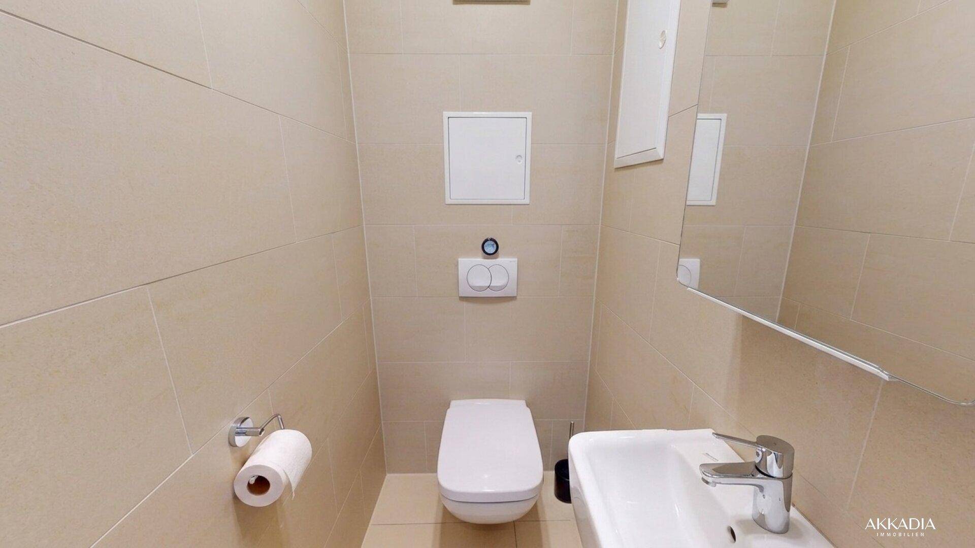 Kompaktes Gäste-WC mit wandhängender Toilette, kleinem Waschbecken und hellen Fliesen.