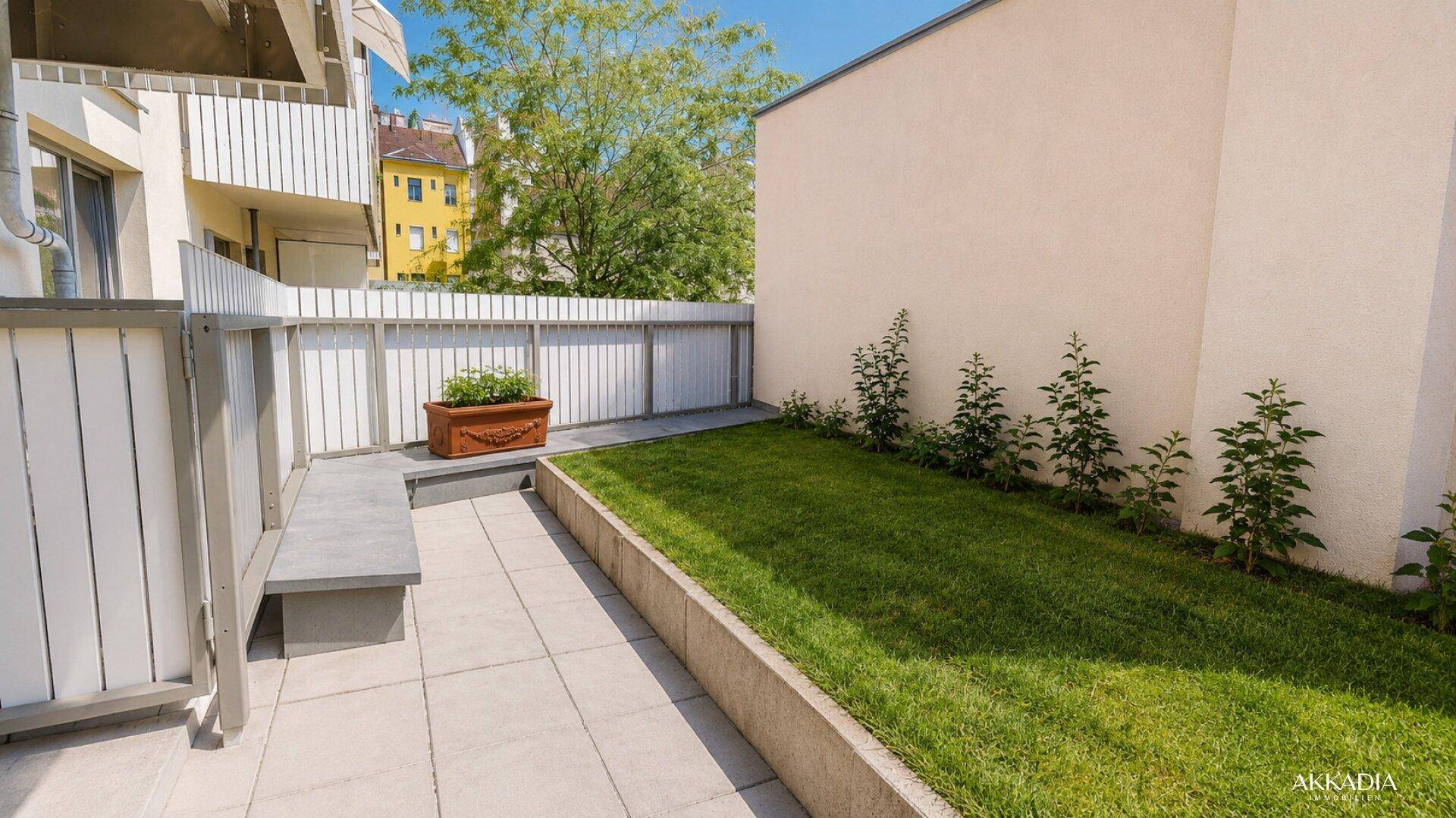 Ruhige Terrasse mit kleiner Rasenfläche und einer fest installierten Sitzbank im Freien.
