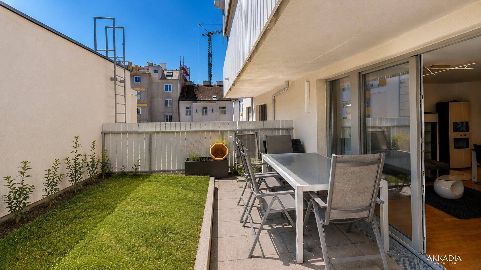 Sonnige Terrasse mit Rasenfläche, Gartenmöbeln und Blick auf die umliegende Bebauung.