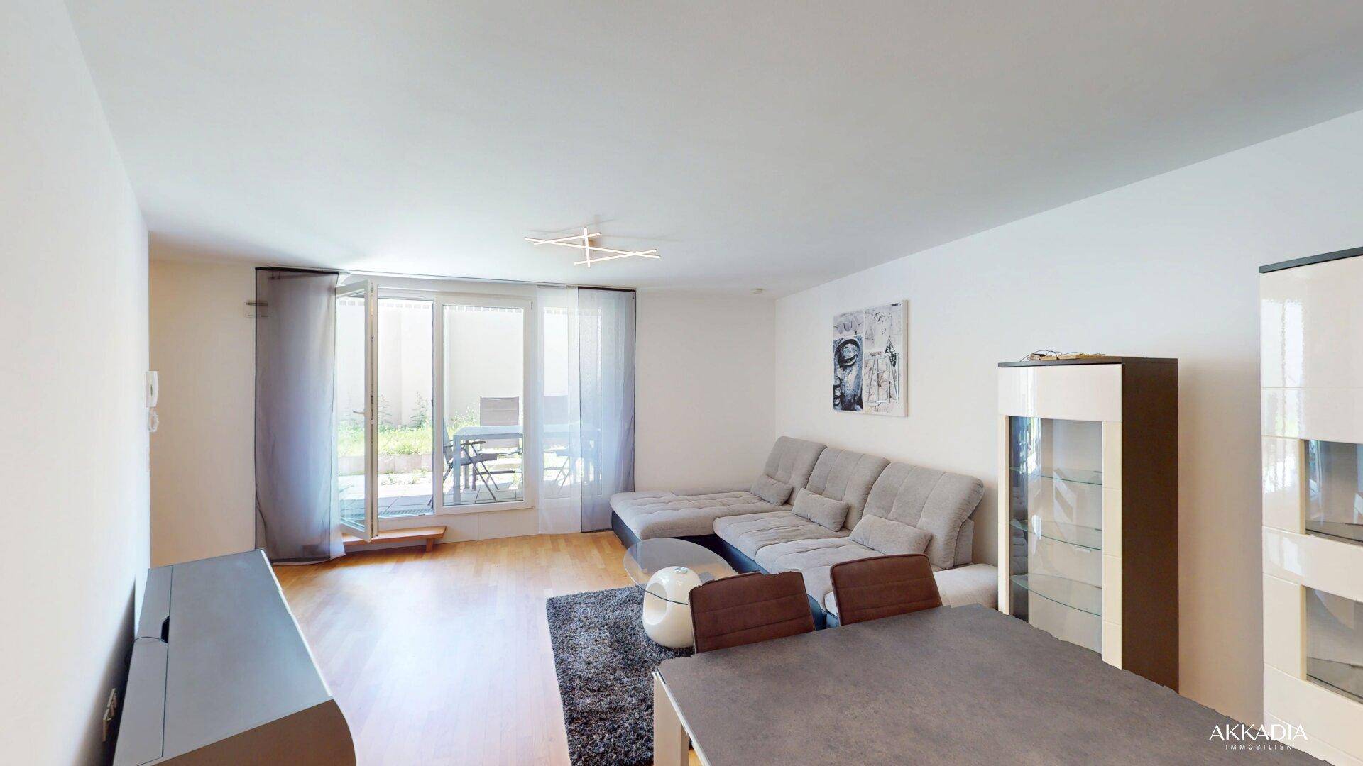 Heller Wohnbereich mit Sofa, Esstisch und großem Fenster mit Zugang zu einem Außenbereich.