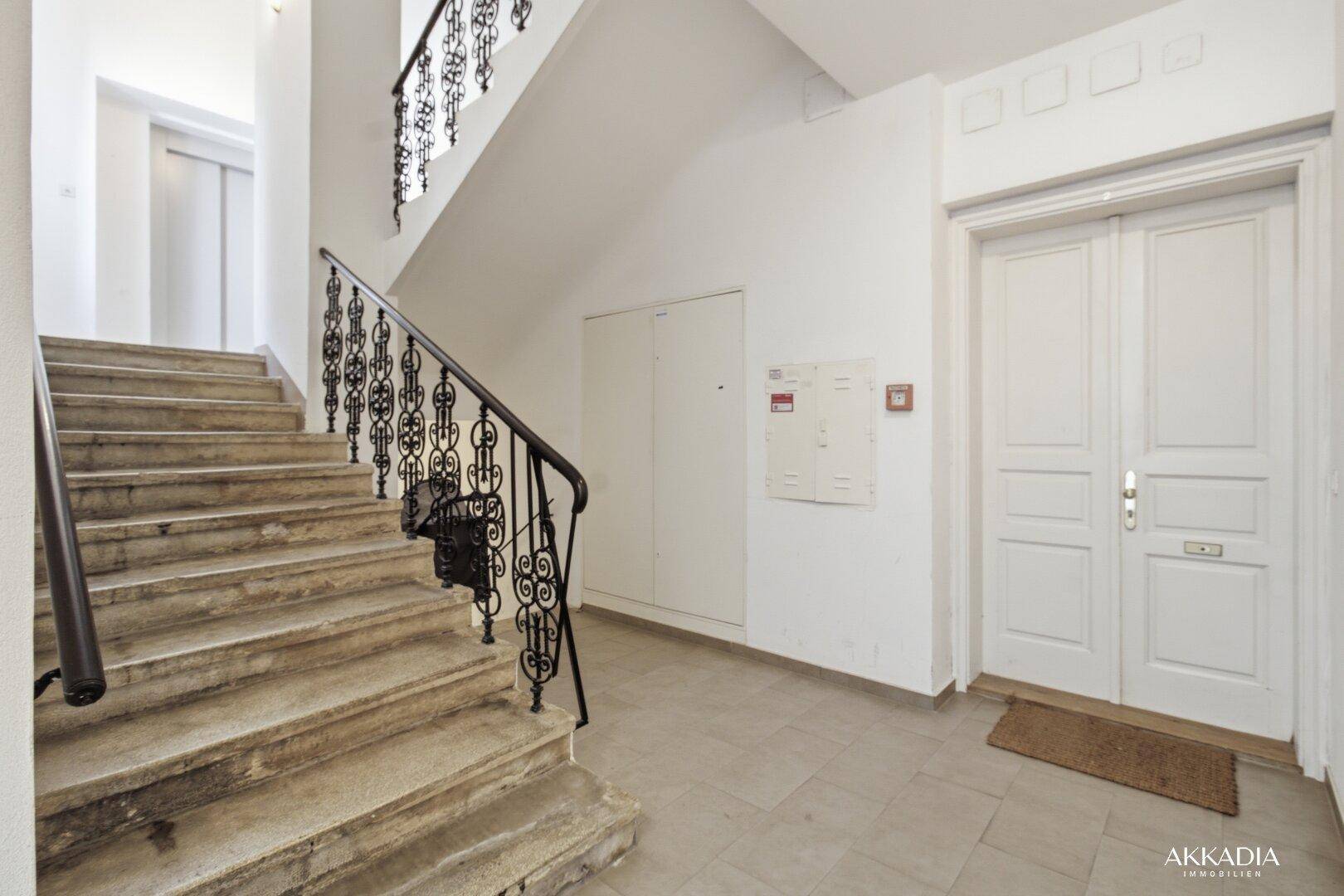 Treppenhaus mit Steinstufen, schmiedeeisernem Geländer und sichtbarem Aufzug.