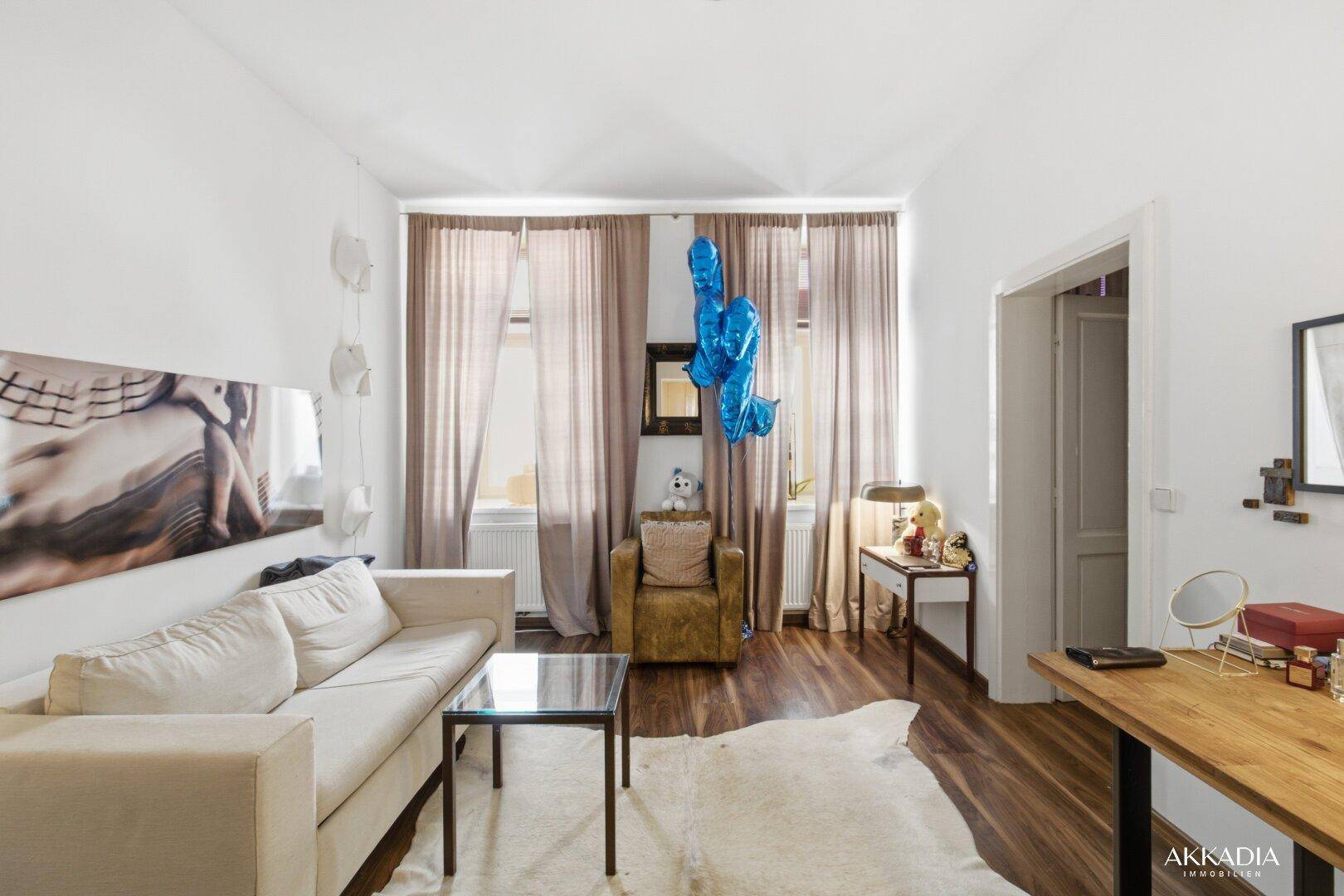 Geräumiges Wohnzimmer mit beigem Sofa, Holzboden und Zugang zu weiteren Räumen.