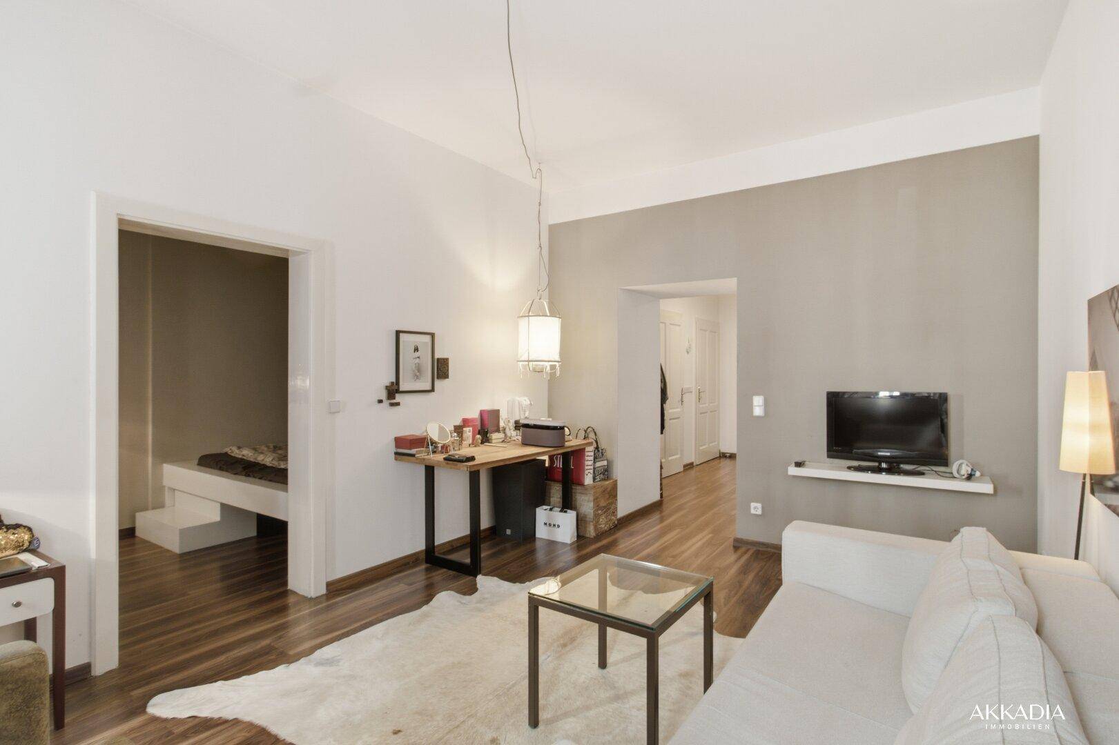 Offener Wohnbereich mit Schreibtisch, Sofa und Blick in ein angrenzendes Schlafzimmer.