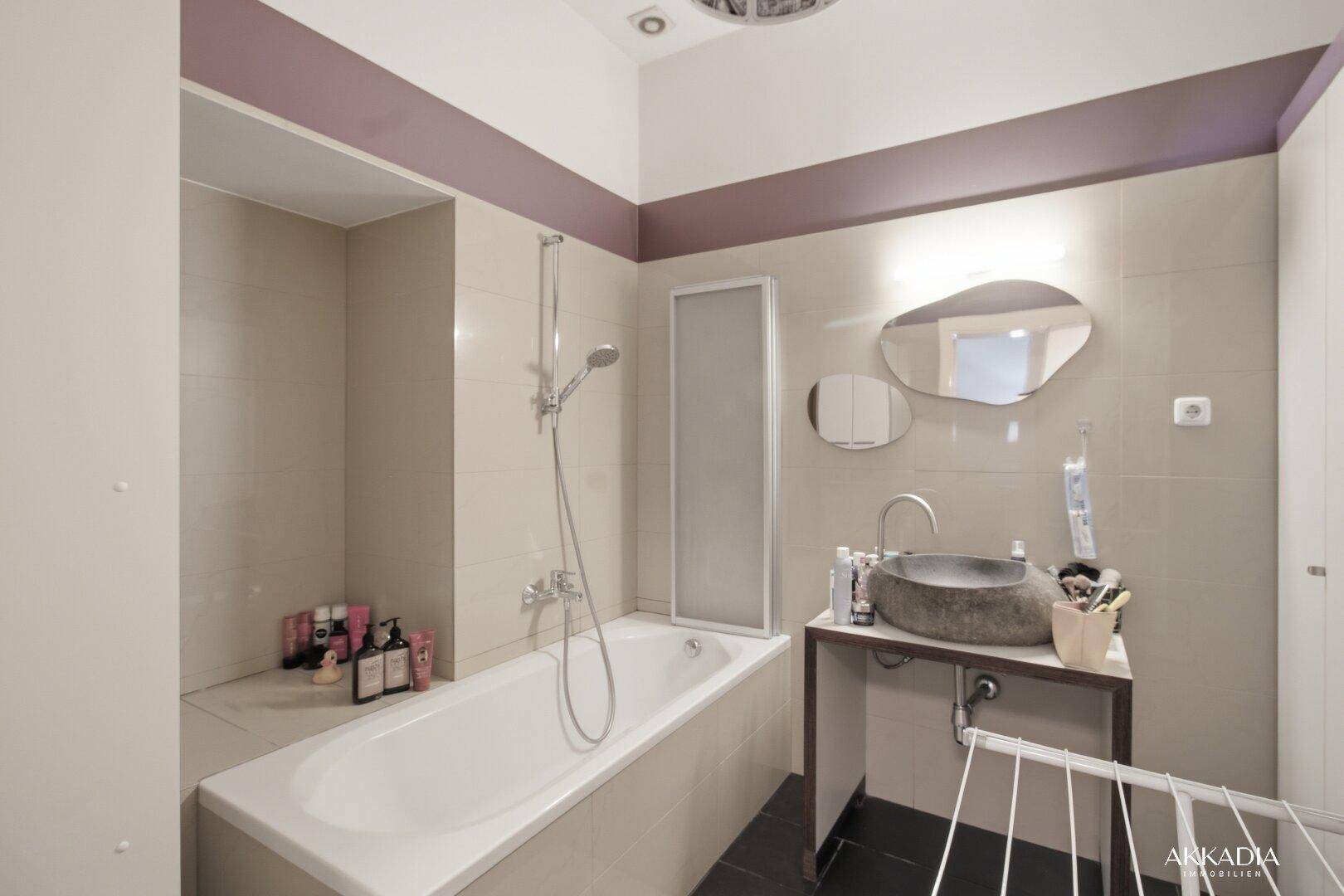 Badezimmer mit Badewanne, modernem Steinwaschbecken und beigefarbenen Fliesen.