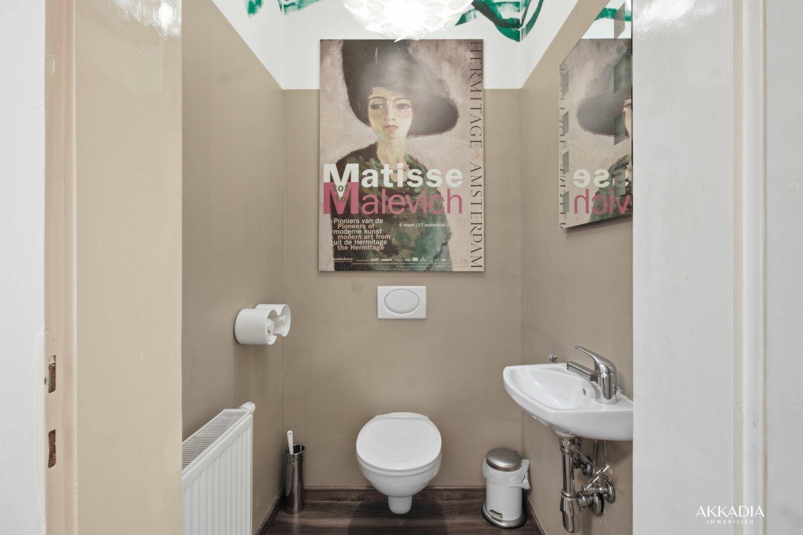 Separates WC mit Toilette, kleinem Waschbecken und dekorativem Poster.