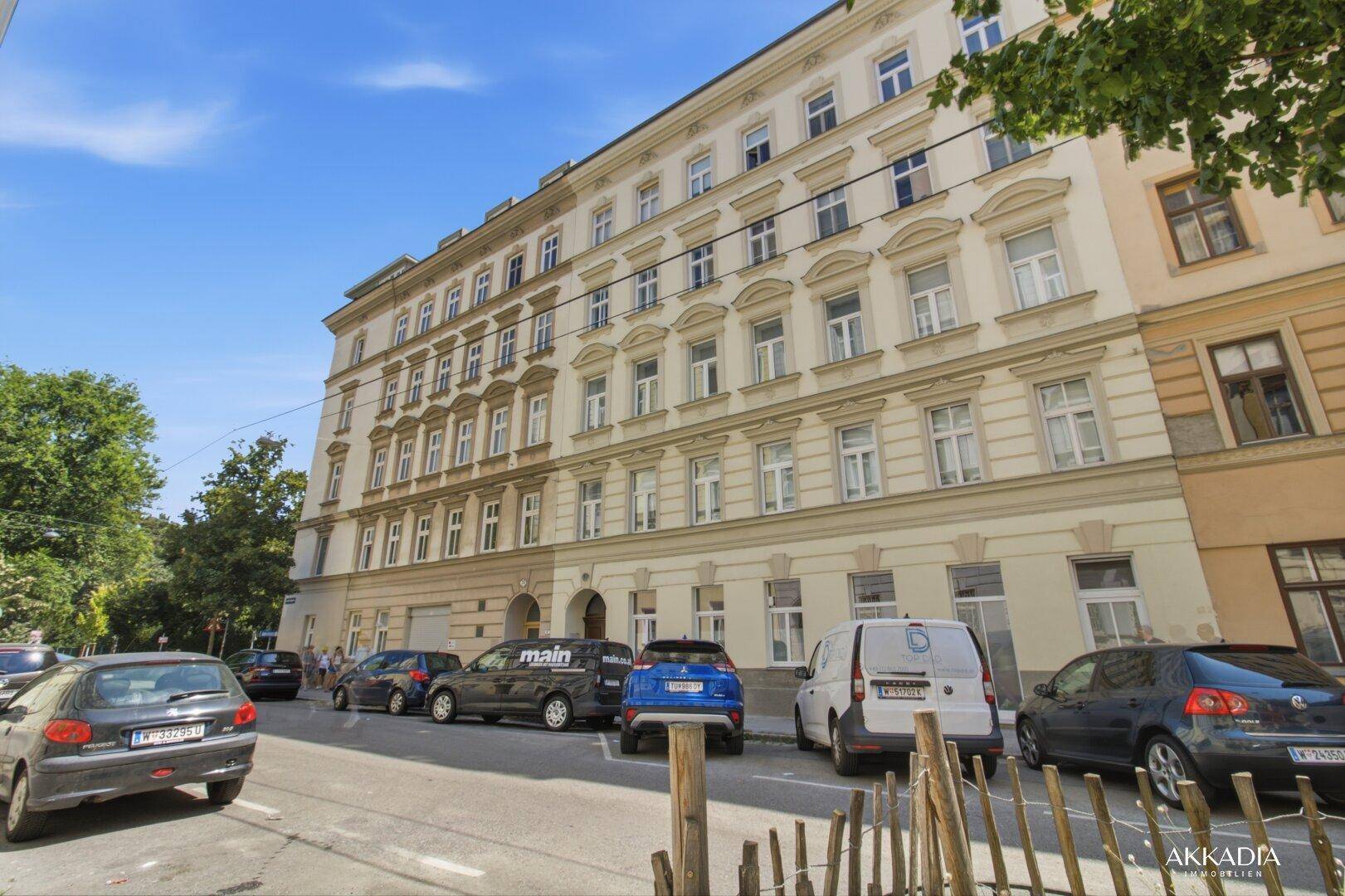 Ansicht der Gebäudefassade von der Straße mit geparkten Fahrzeugen und Bäumen.