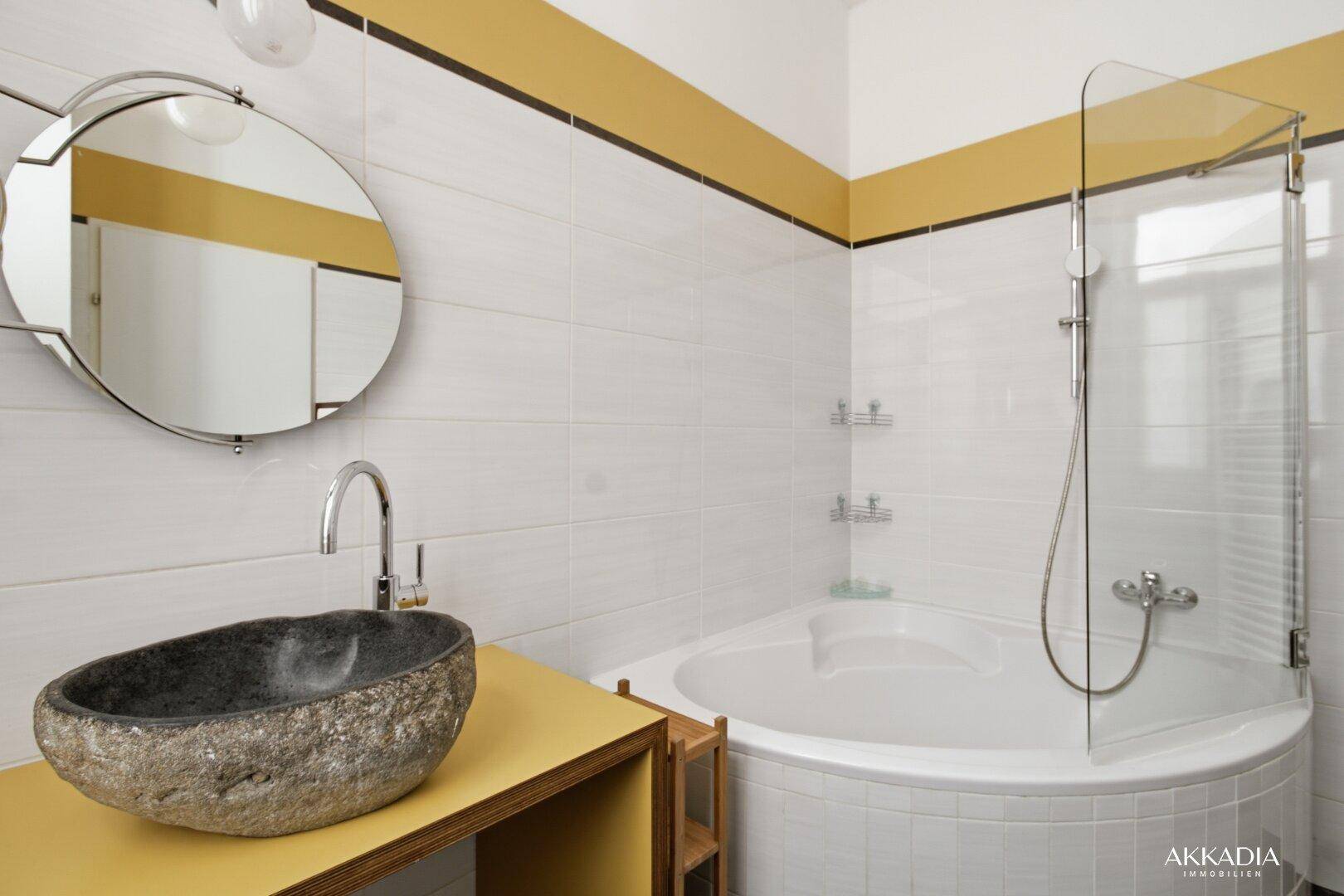 Modernes Badezimmer mit Eckbadewanne, Natursteinwaschbecken und gelben Akzenten.