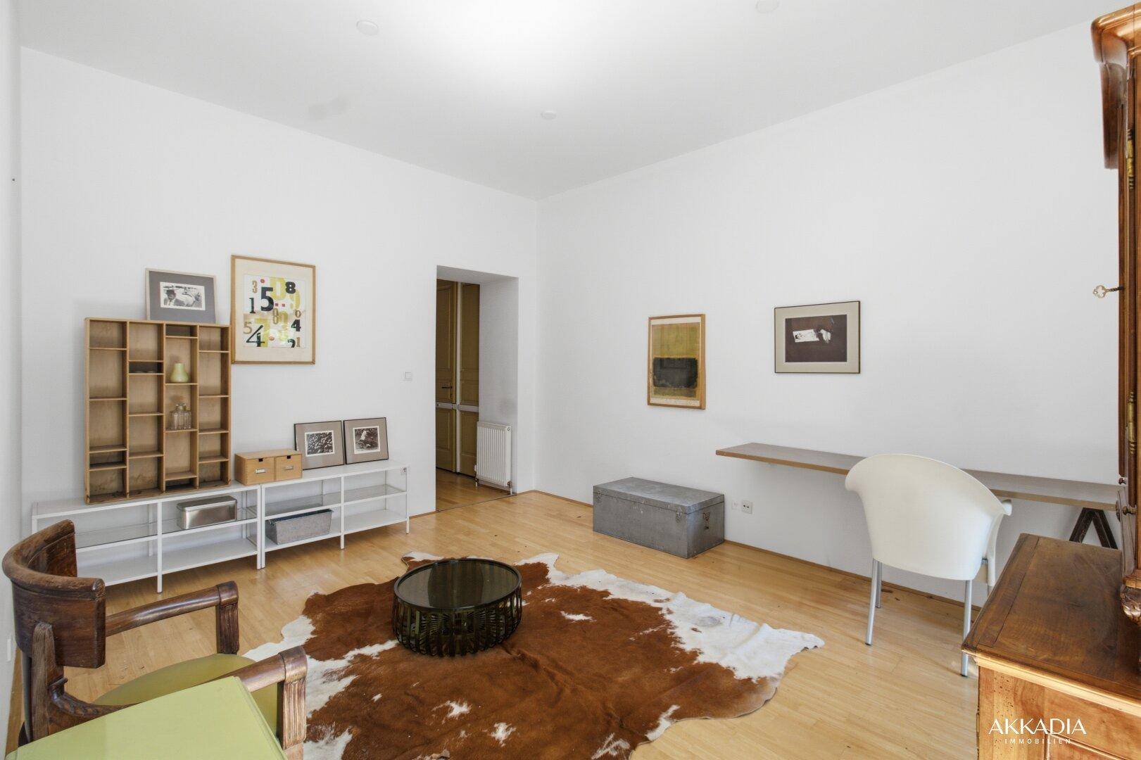 Geräumiges Wohnzimmer mit hellem Holzboden, modernen Möbeln und viel Tageslicht.