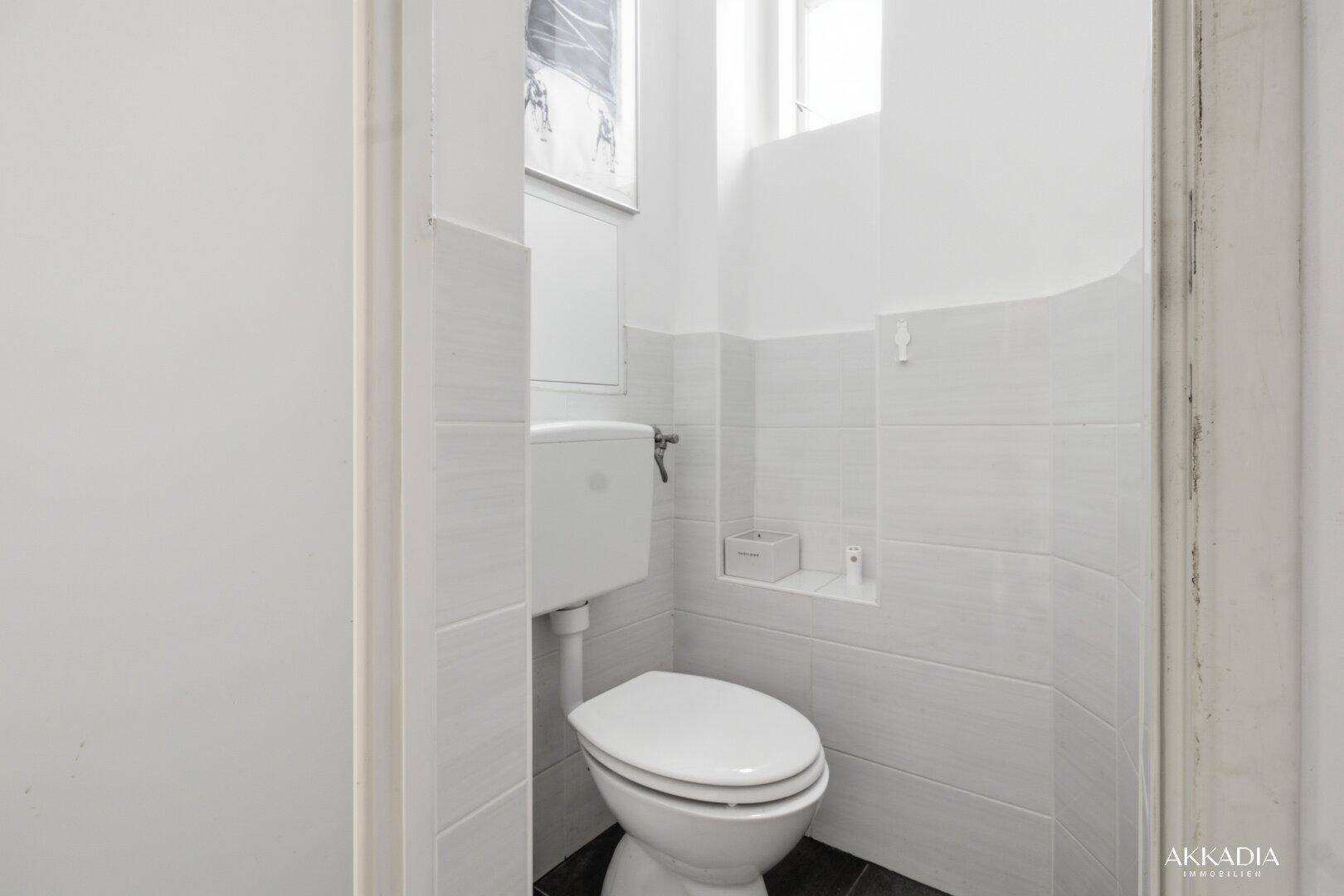 Separates WC mit weiß gefliesten Wänden und schlichtem Design.