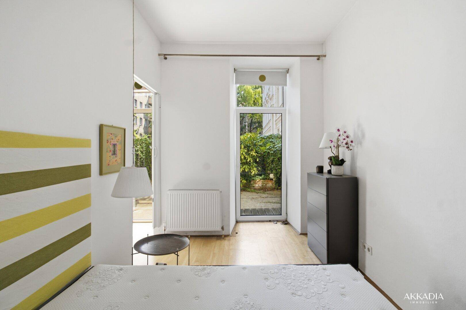 Helles Schlafzimmer mit Kommode, Heizkörper und Zugang zum Außenbereich.