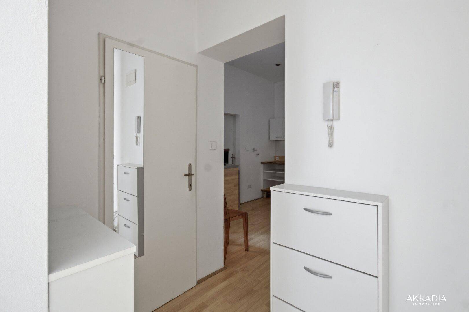 Heller Flur mit Schuhschrank, Gegensprechanlage und Spiegeltür.