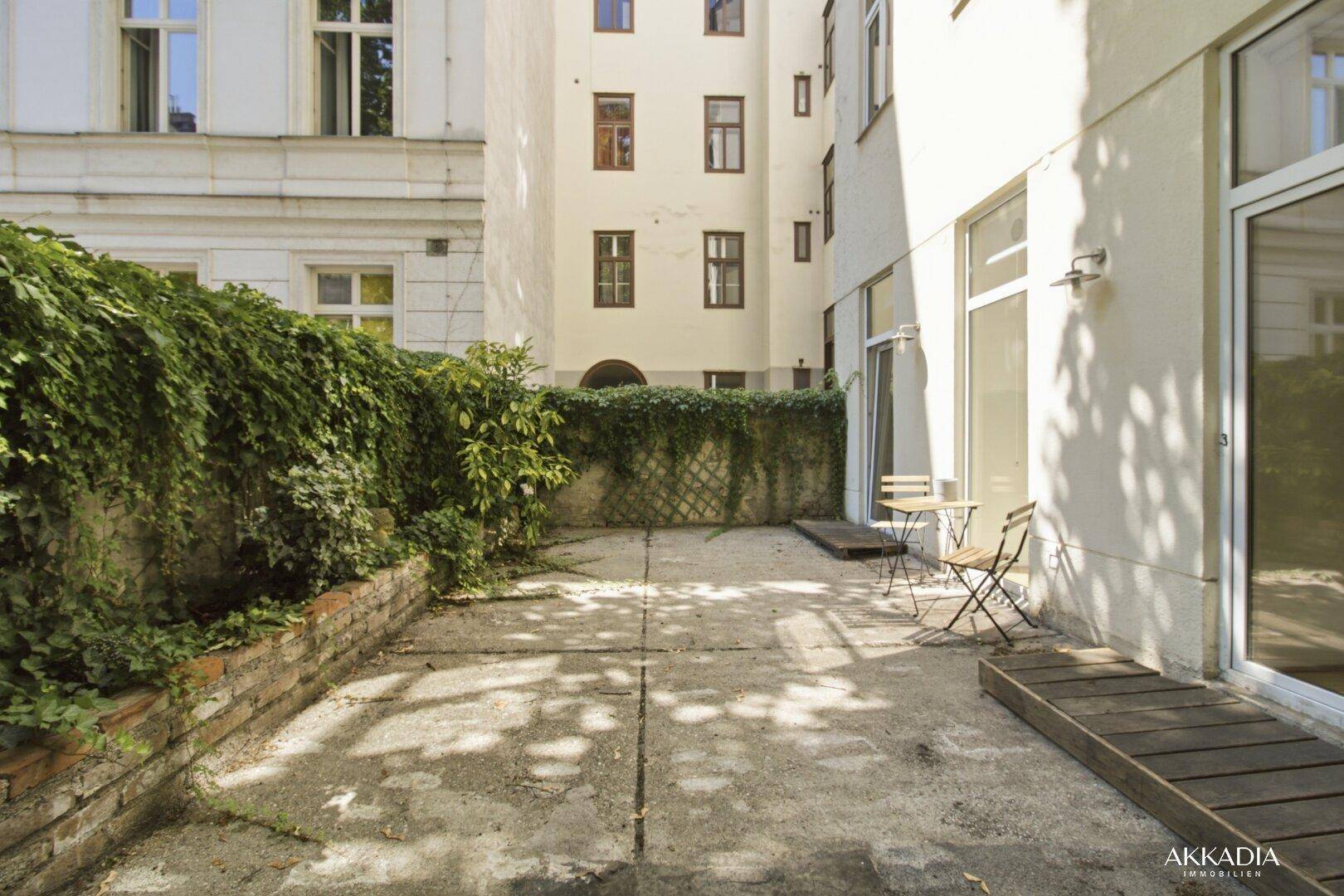 Gemütliche Terrasse mit Sitzgelegenheiten, umgeben von begrünten Mauern und Gebäuden.