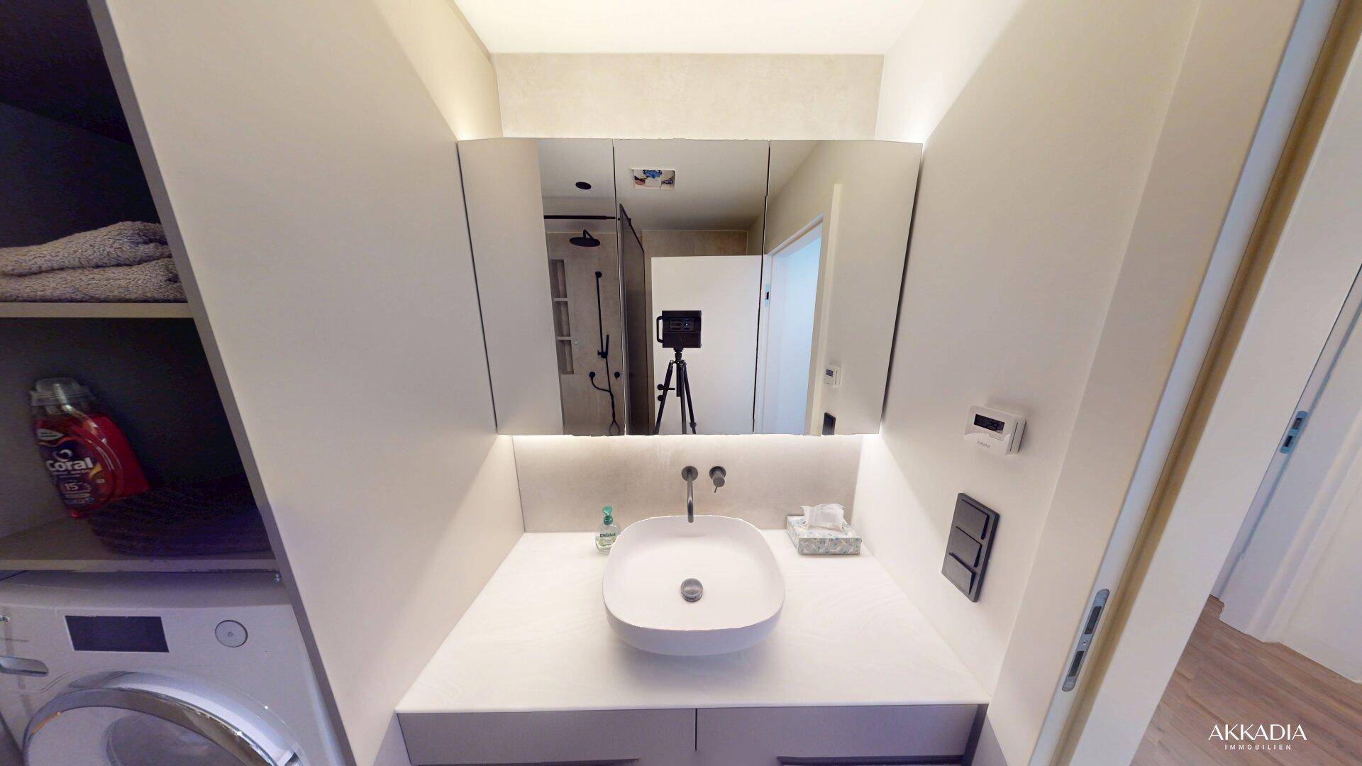 Funktionales Badezimmer mit Waschbecken, Spiegelschrank und integrierter Waschmaschine, praktisch eingerichtet.