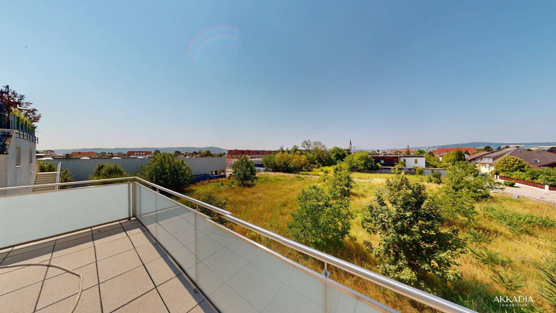 Großzügige Dachterrasse mit Fliesenboden und Glasgeländer, bietet weiten Blick ins Grüne.