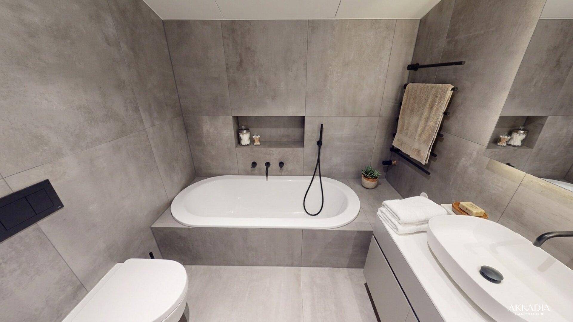 Modernes Badezimmer mit integrierter Badewanne, wandhängendem WC und eleganten grauen Fliesen.