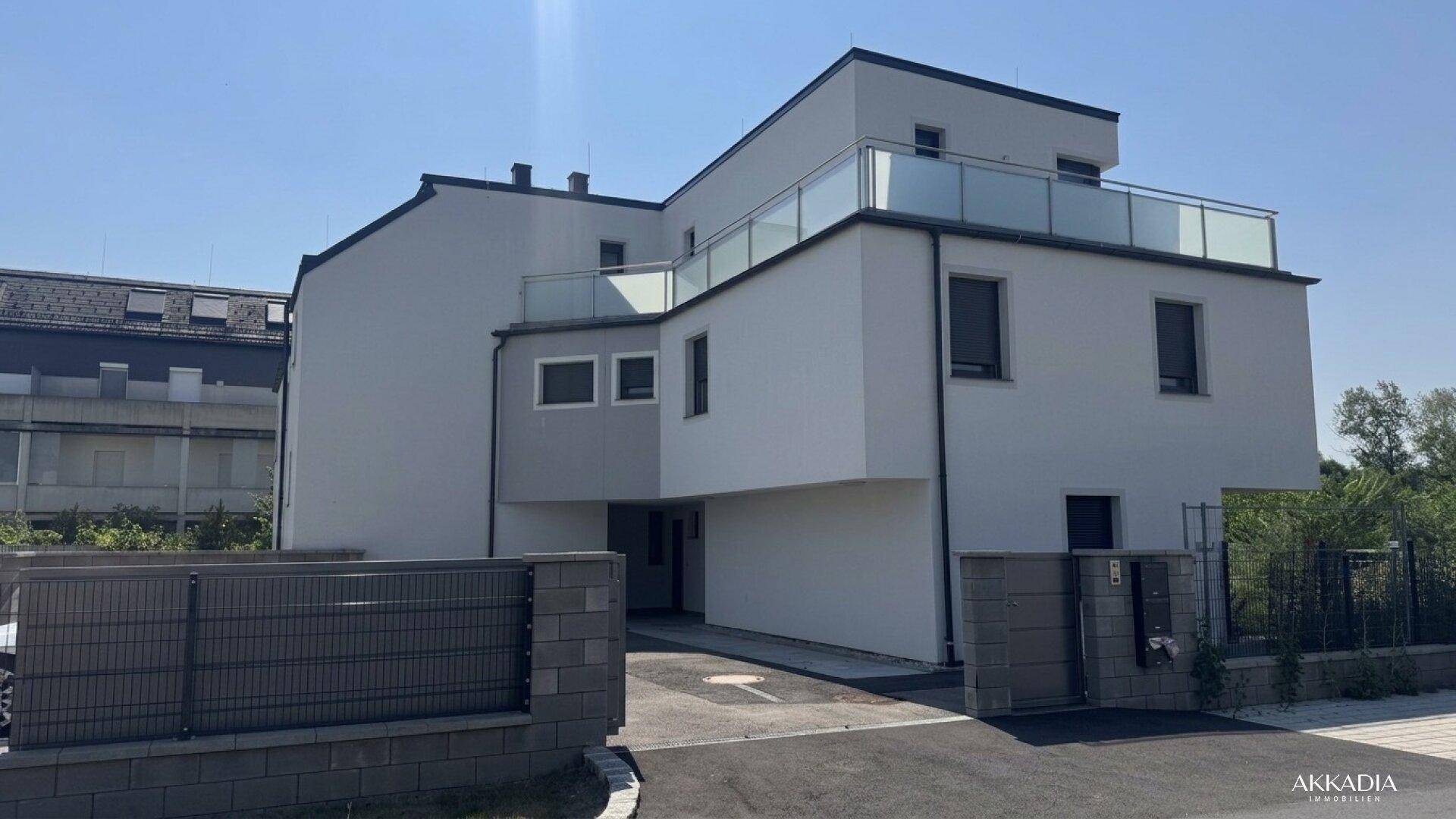 Moderne Wohnanlage mit weißer Fassade, großen Fenstern und Balkonen unter blauem Himmel.