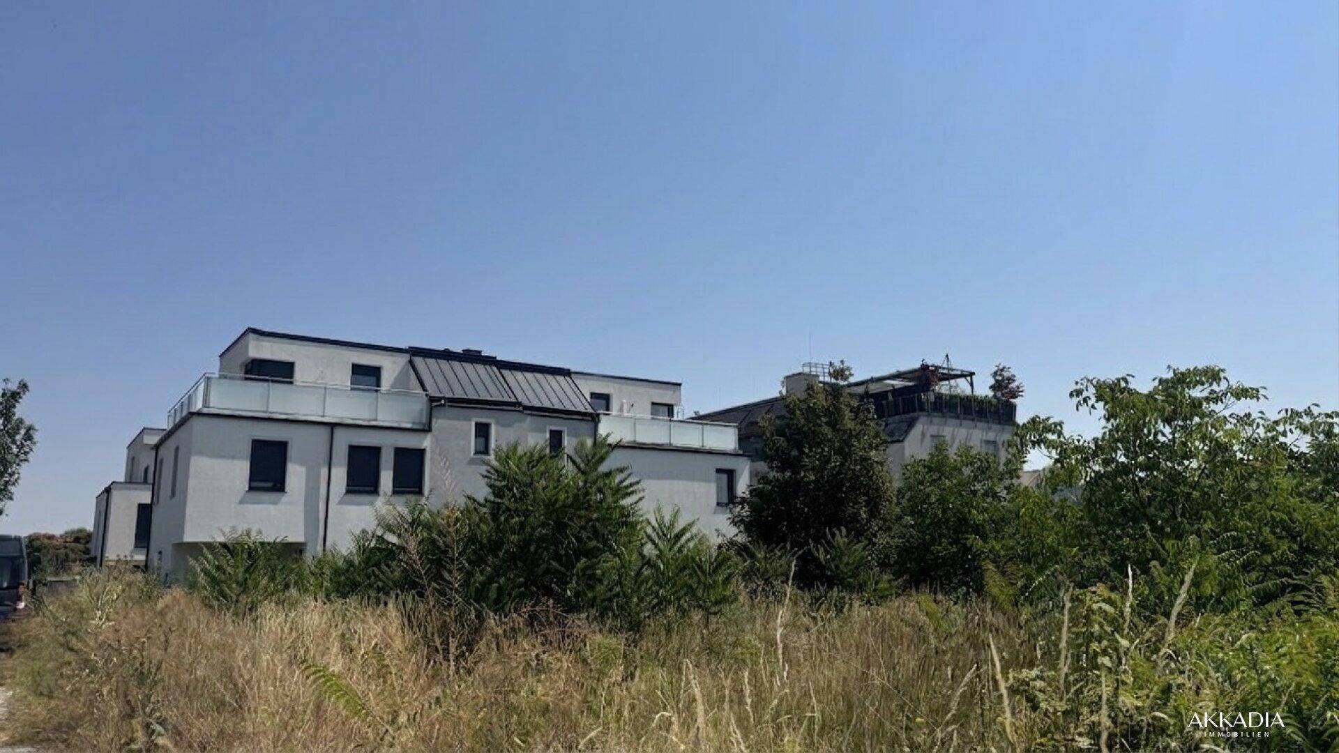 Moderne Wohngebäude in grüner Umgebung, umgeben von Bäumen und Wiesen unter klarem Himmel.