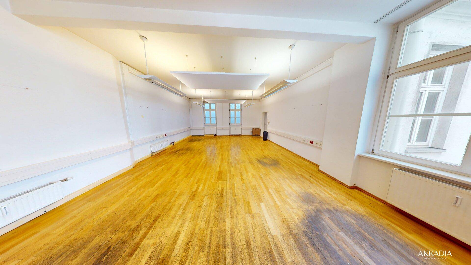 Weitläufiger Büroraum mit Holzparkett, hohen Decken und großen Fenstern für viel Tageslicht und eine offene Atmosphäre.