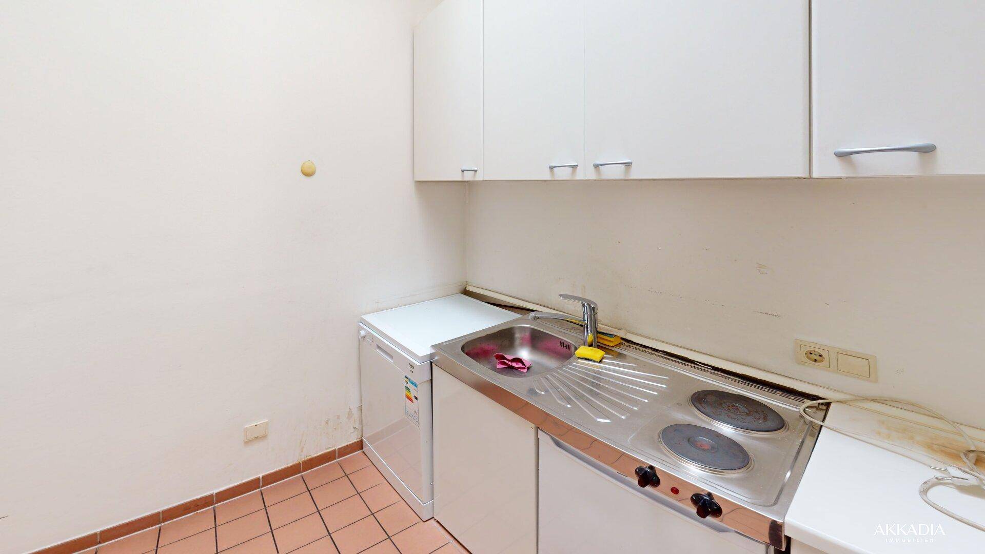 Kleine Küchenzeile mit Spüle, Kochplatten, Kühlschrank und weißen Hängeschränken, praktisch und funktional.