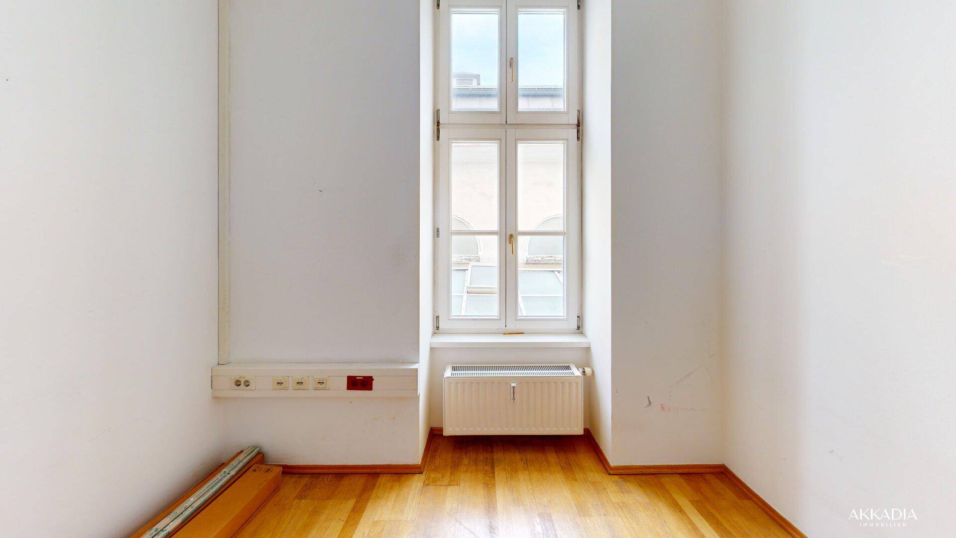 Kleiner Büroraum mit einem hohen Fenster, weißen Wänden und einem hellen Holzfußboden, ideal für Einzelbüros.