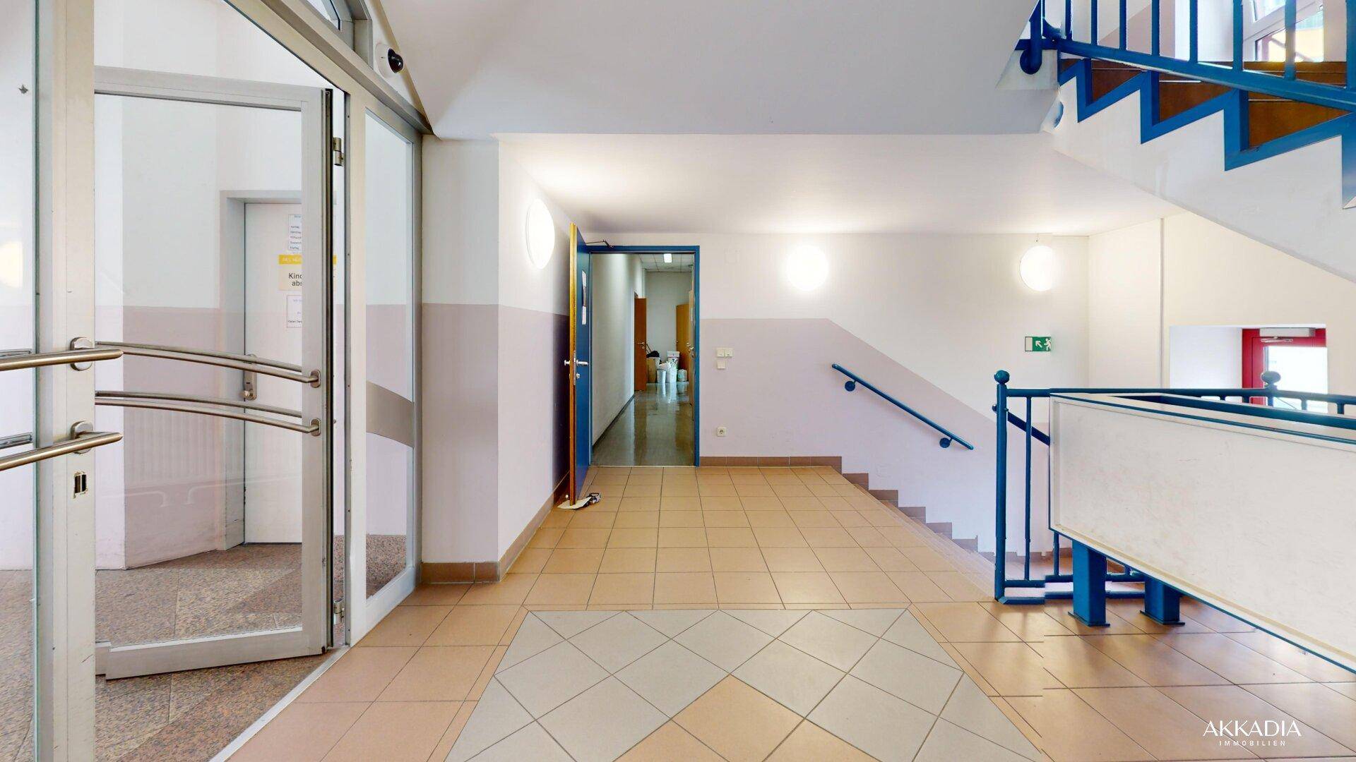 Eingangsbereich mit Treppe, gefliestem Boden und einer Glastür, die ins Freie führt.
