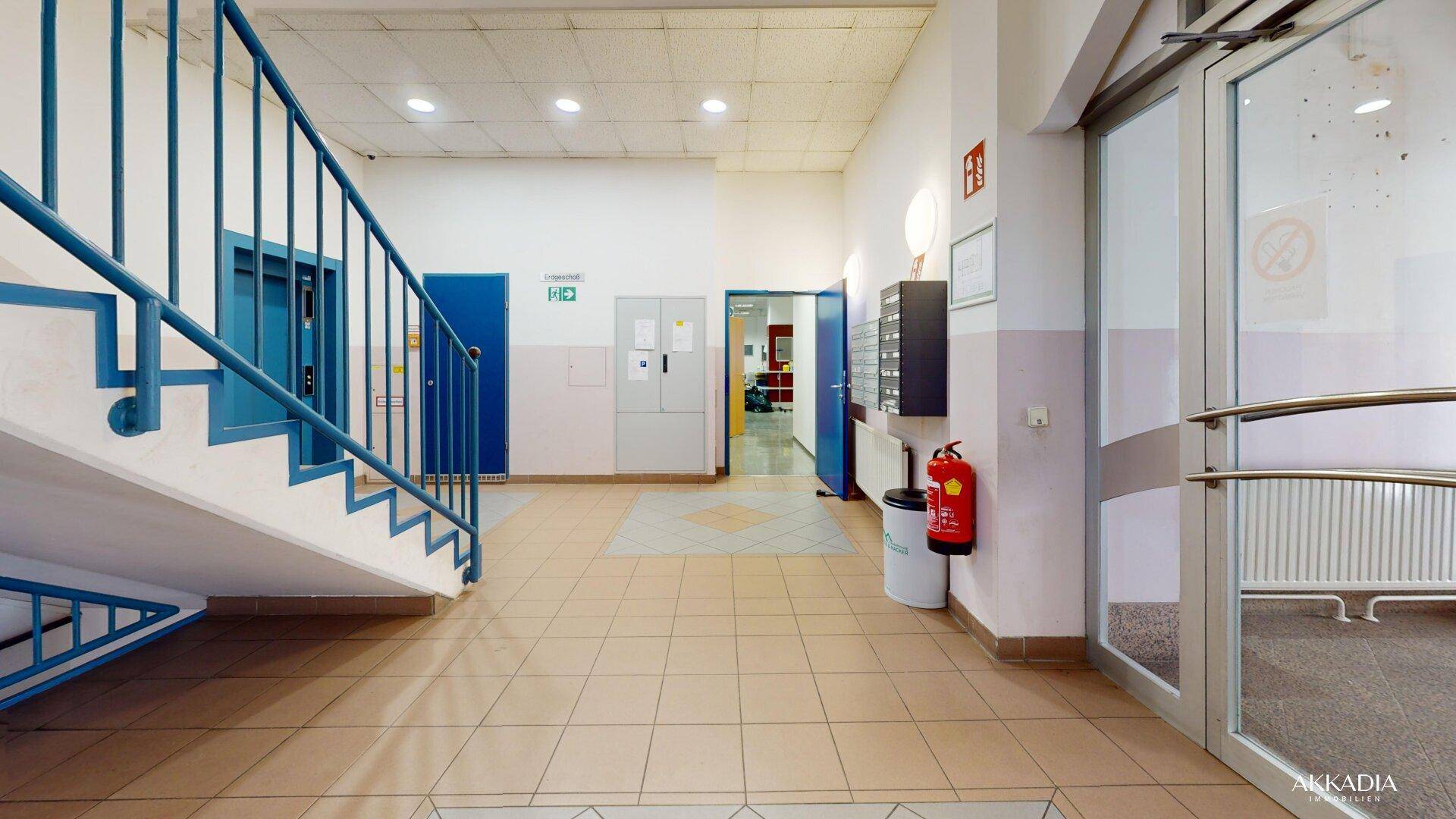 Eingangsbereich mit Treppe, Aufzug und gefliestem Boden in einem Geschäftsgebäude.