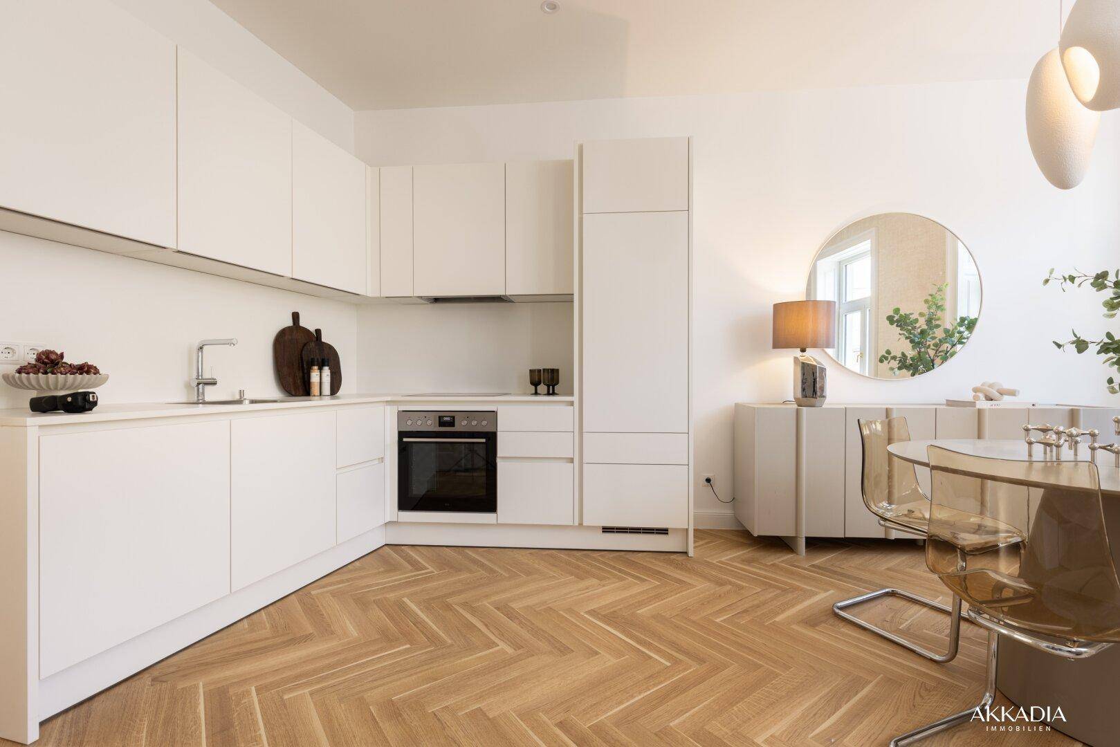 Moderne, offene Küche mit weißen Schränken, integrierten Geräten und Fischgrätparkettboden.