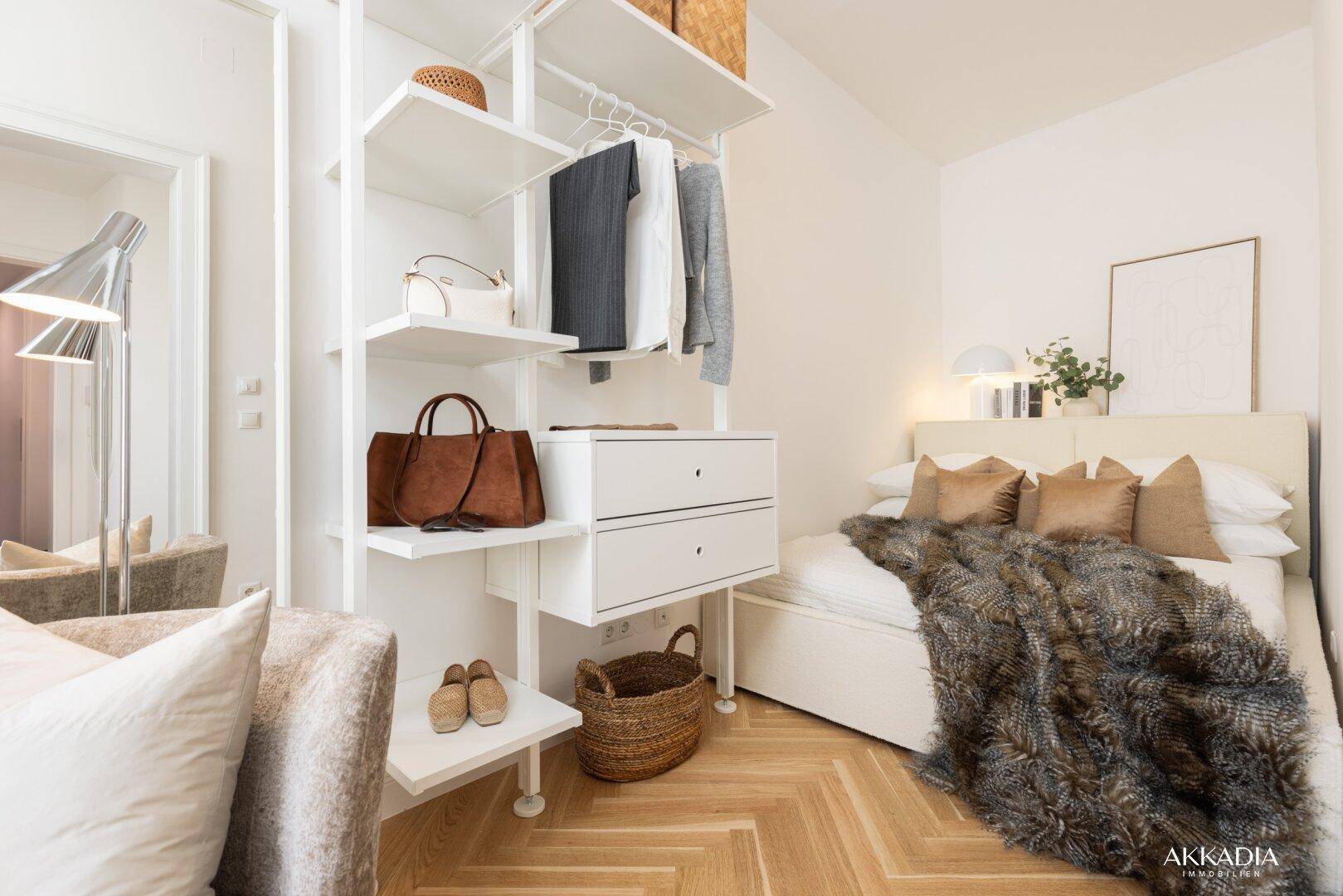 Helles Schlafzimmer mit Doppelbett, offenem Schranksystem und Fischgrätparkettboden.