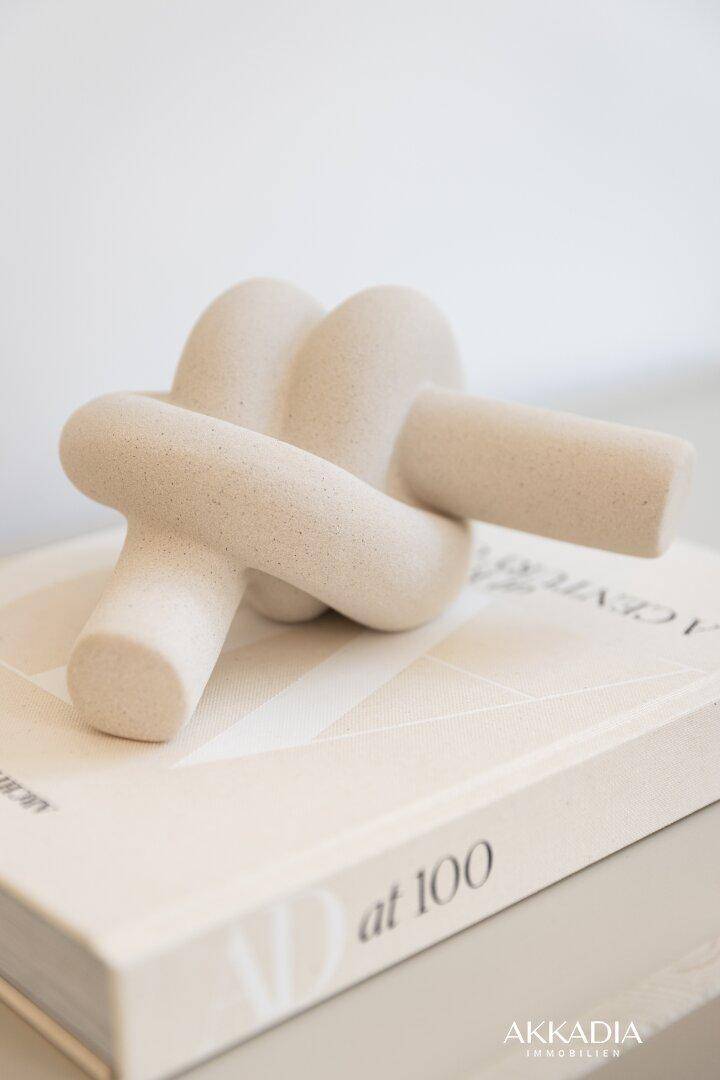 Detailaufnahme einer beigen, skulpturalen Dekoration auf einem Buch, die einen Knoten darstellt.