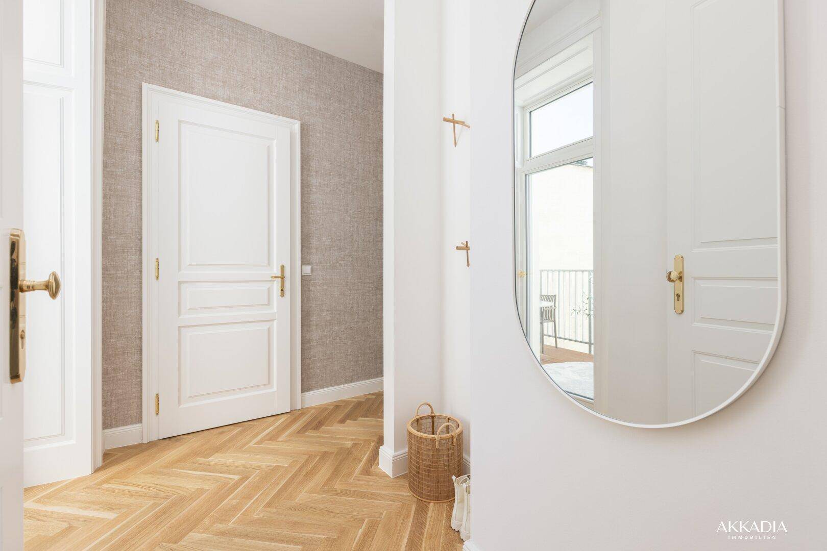 Heller Flur mit elegantem Fischgrätparkett, weißen Türen und einem ovalen Wandspiegel.