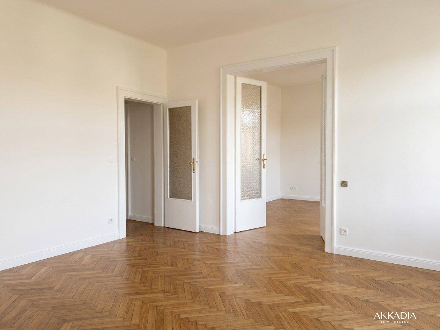 Heller Raum mit Fischgrätparkett und mehreren Türen, die zu angrenzenden Zimmern führen.