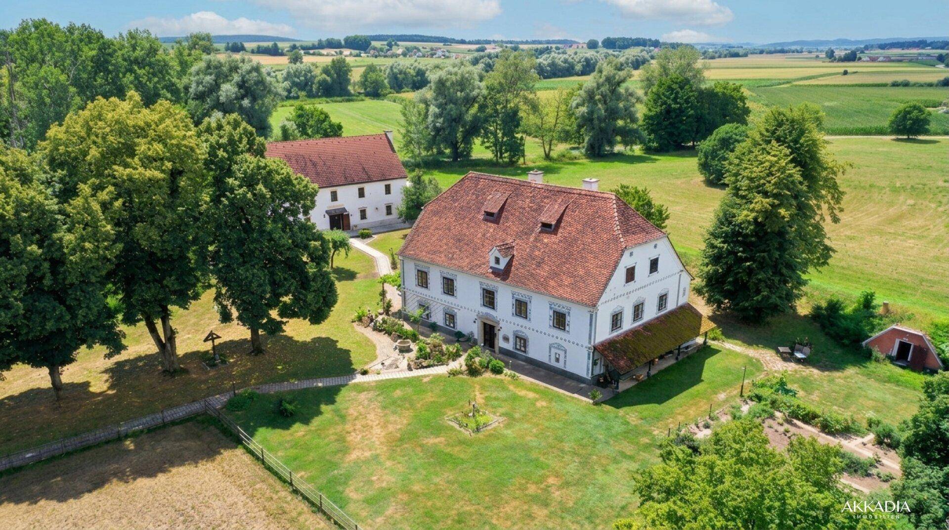 Weitläufiges Anwesen mit mehreren Gebäuden, umgeben von Feldern und Bäumen unter sonnigem Himmel.