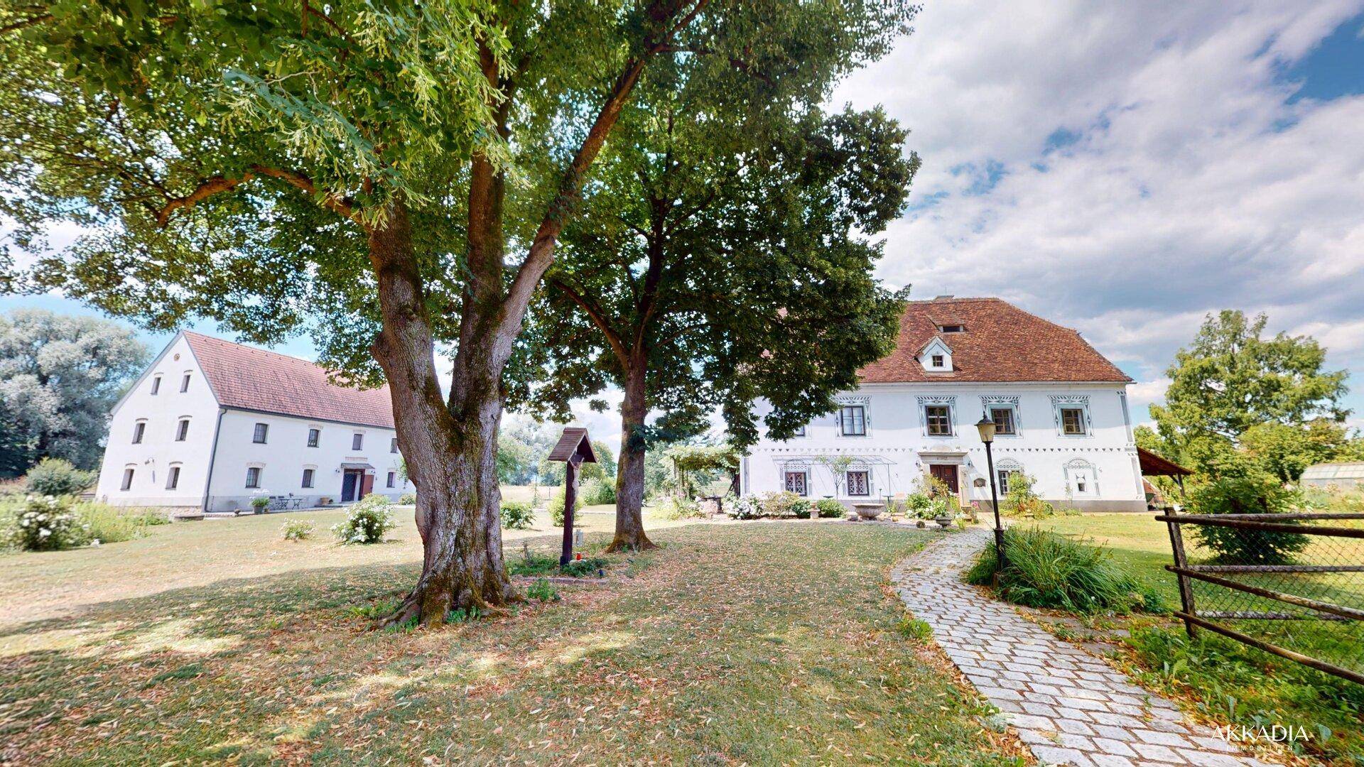 Historisches Anwesen mit gepflegtem Garten, alten Bäumen und einem gepflasterten Weg.