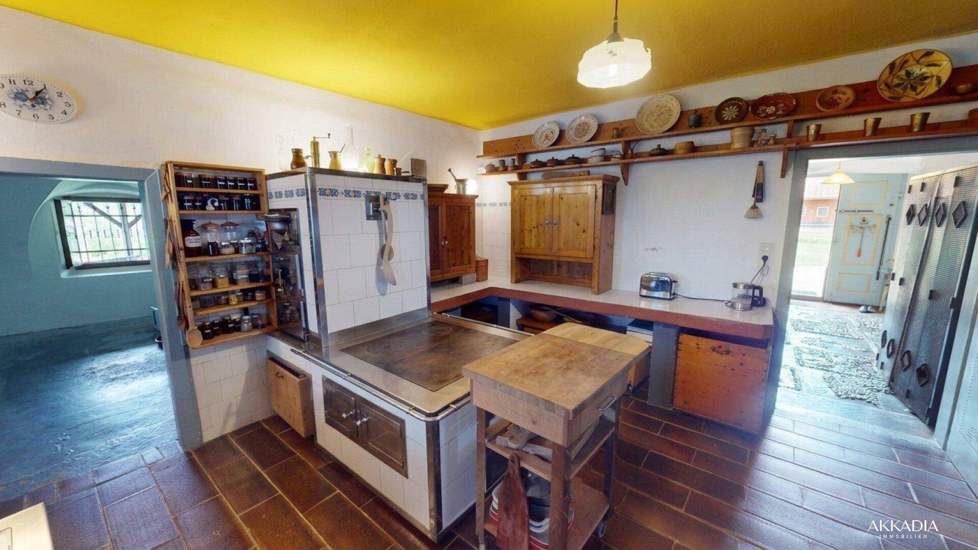 Rustikale Küche mit traditionellem Kachelofen, Terrakottaboden und gelber Decke.