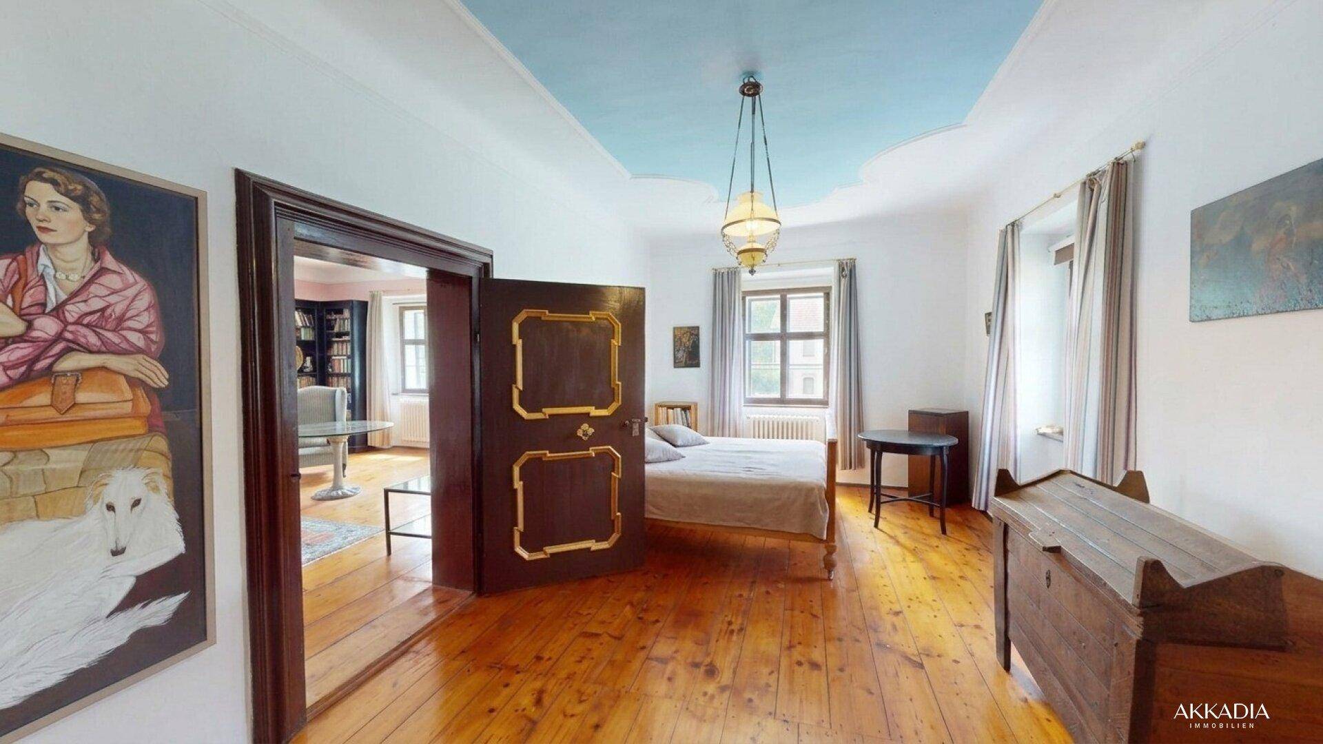 Helles Schlafzimmer mit Holzboden, blauer Deckenmalerei und antiken Türen.