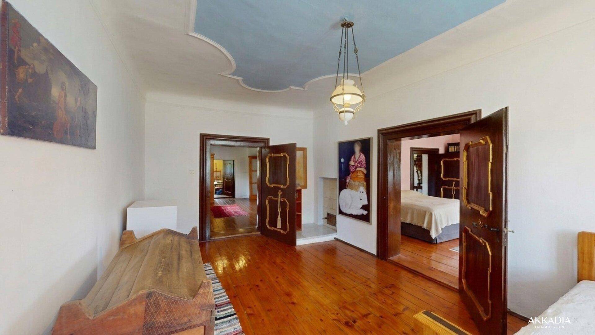 Großes Schlafzimmer mit Holzboden, blauer Deckenmalerei und antiken Türen.