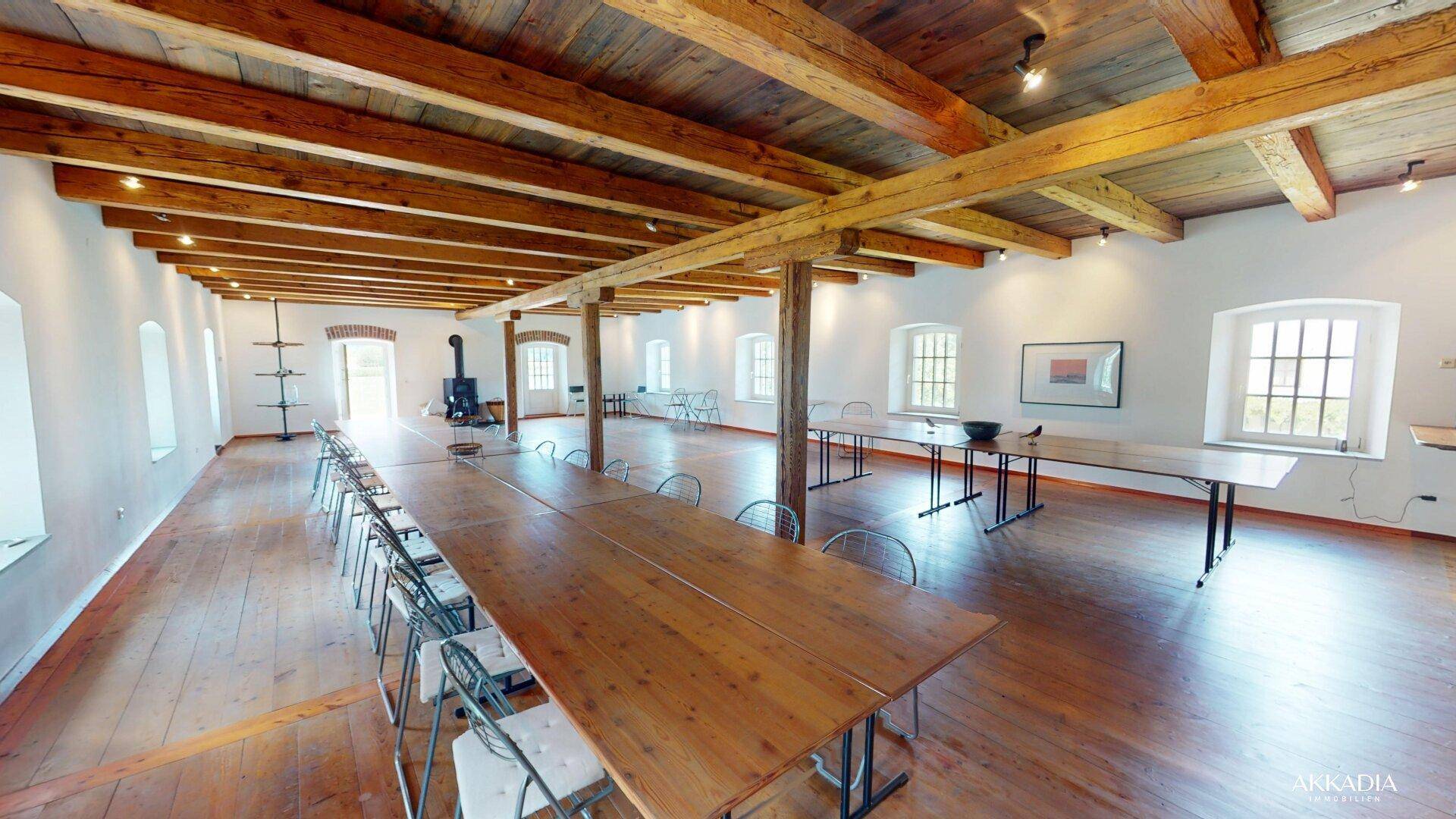 Großer Saal mit Holzbalkendecke, Holzboden und langen Tischen, ideal für Veranstaltungen.